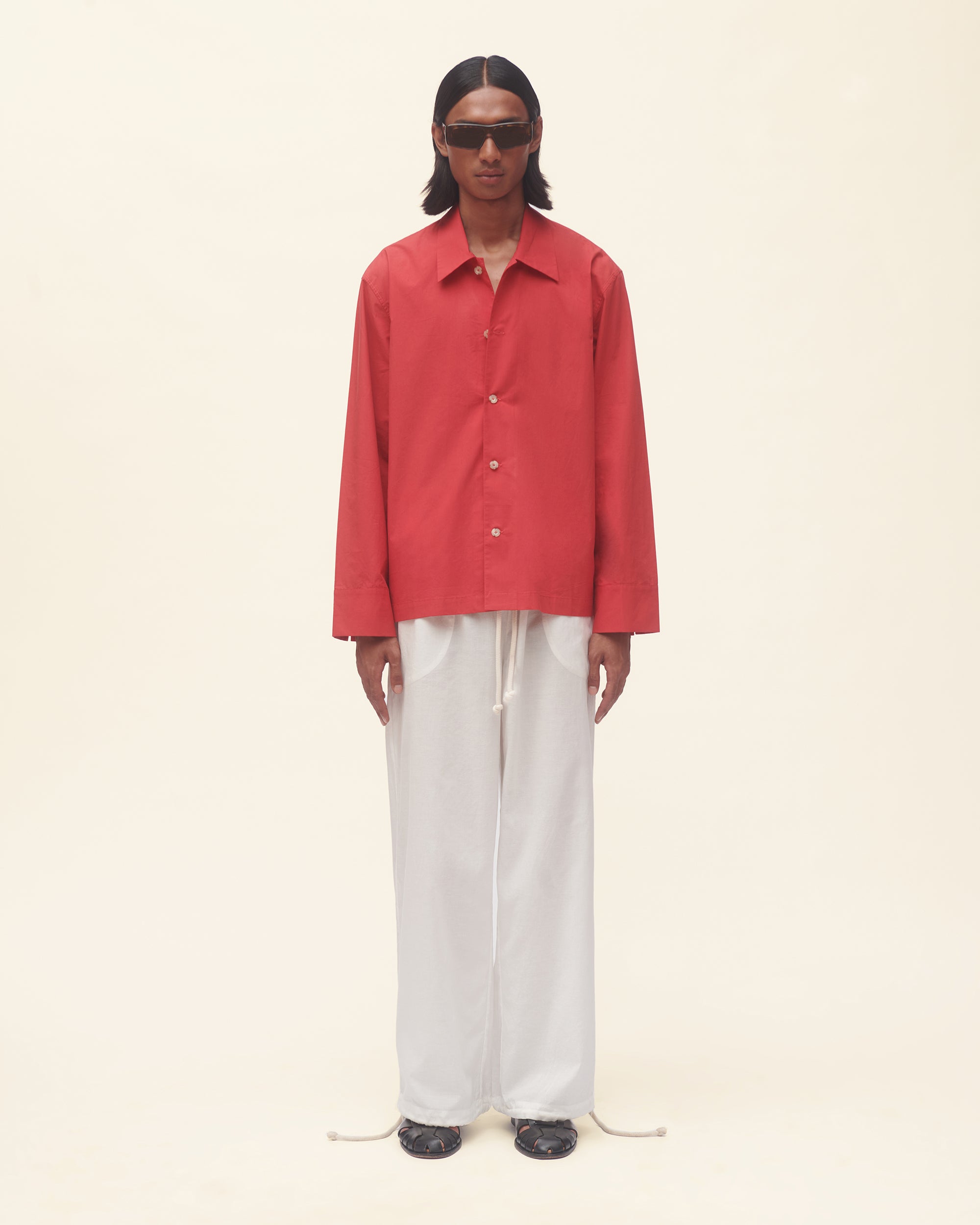 Person wearing a red shirt and white pants on a beige background