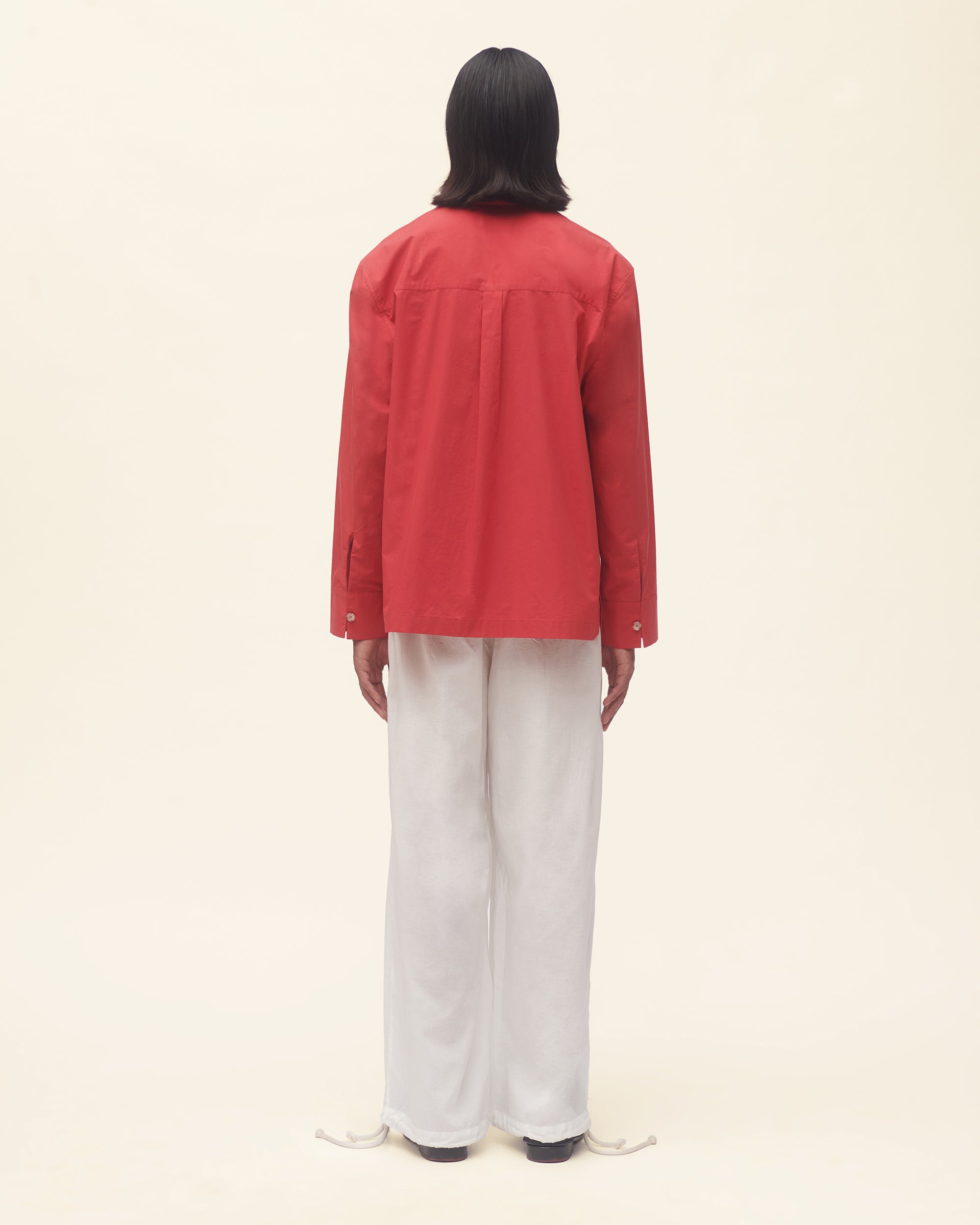 Person wearing a red shirt and white pants on a beige background
