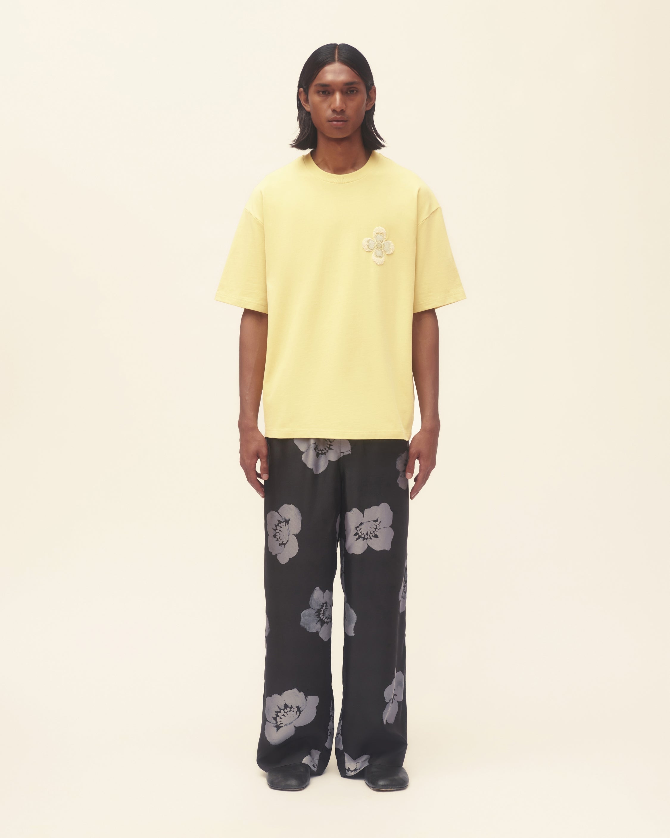Person wearing a yellow t-shirt and black floral pants on a beige background