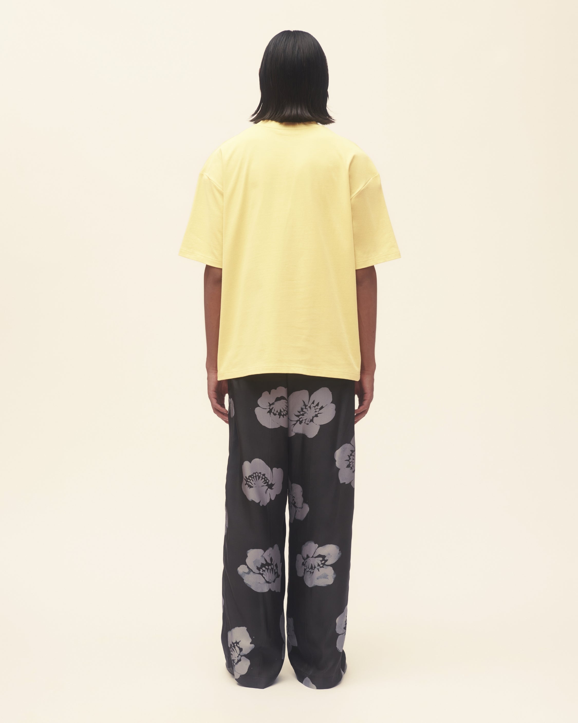 Person wearing a yellow t-shirt and black floral pants on a beige background