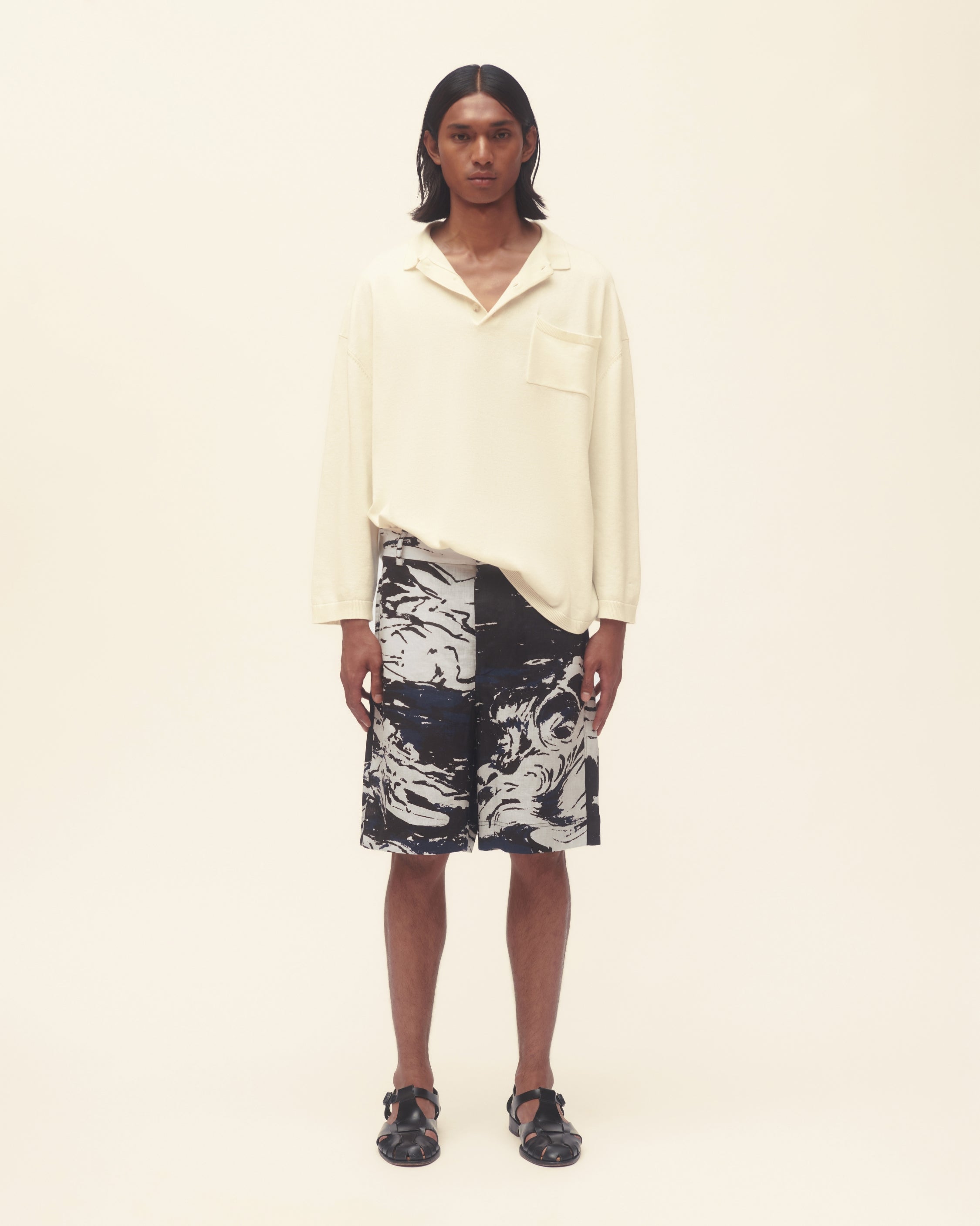 Person wearing a light-coloured shirt and patterned shorts on a plain background