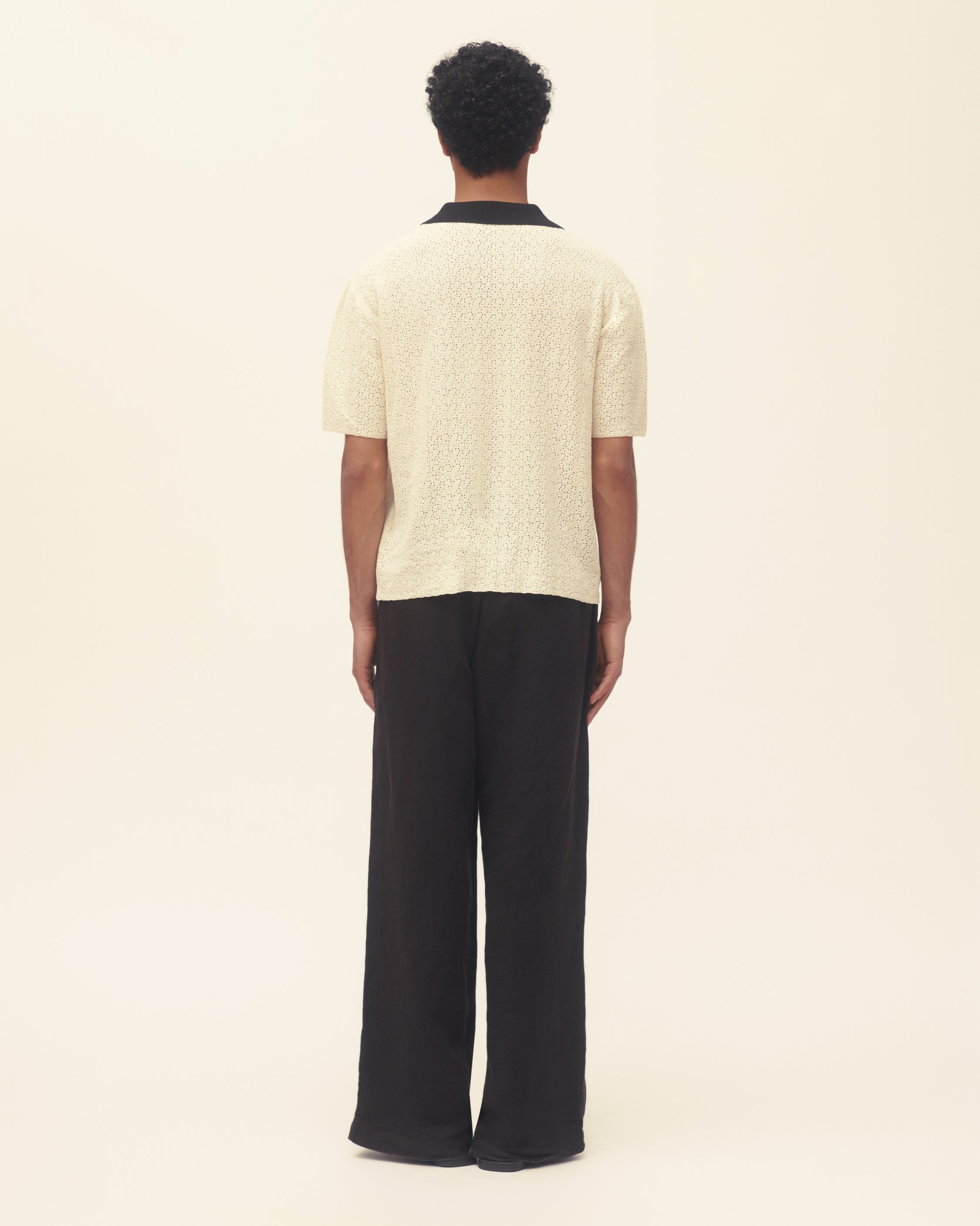 Person wearing a cream crochet polo and black pants on a white background