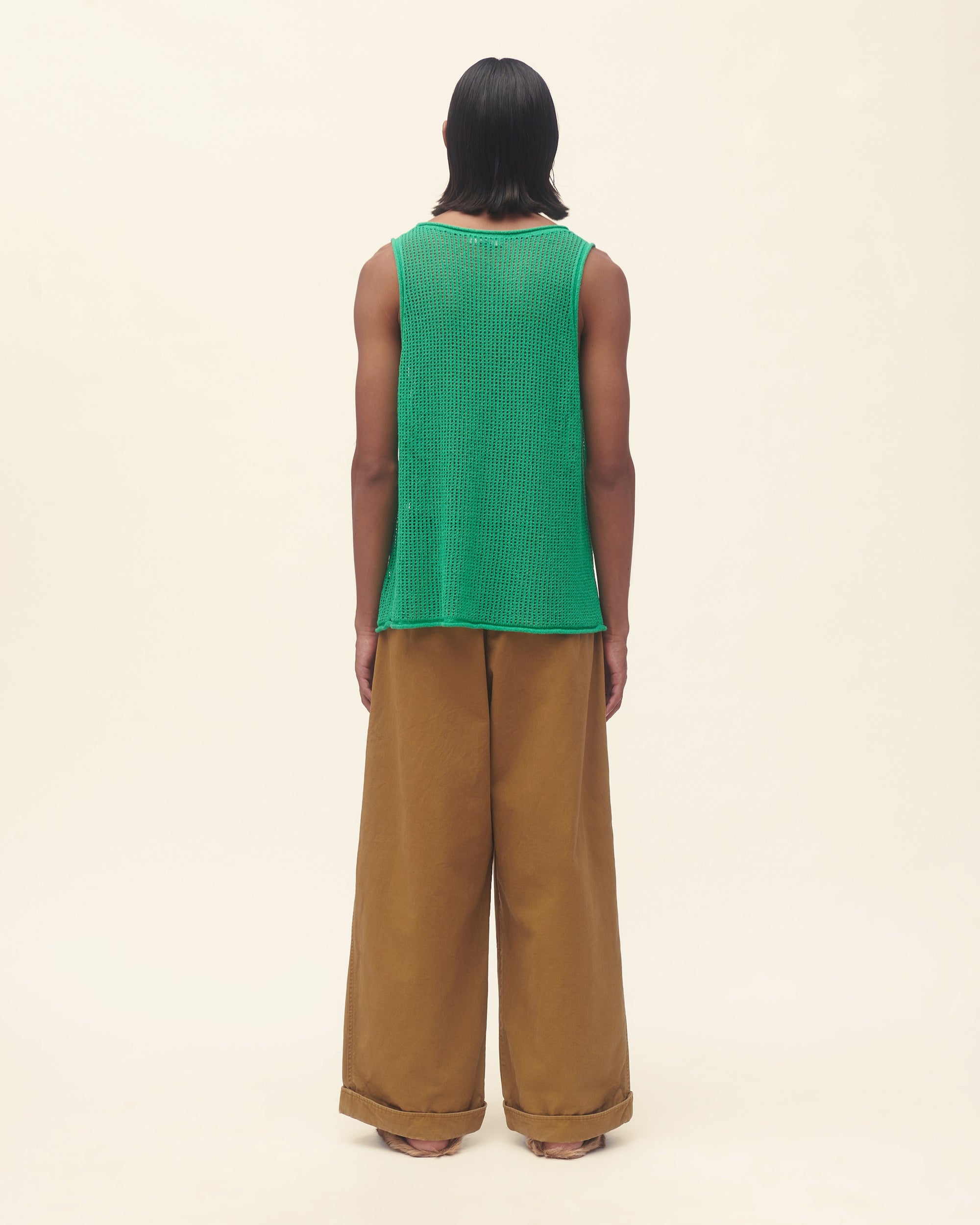 Person wearing a green sleeveless top with blue floral patterns and brown pants on a beige background