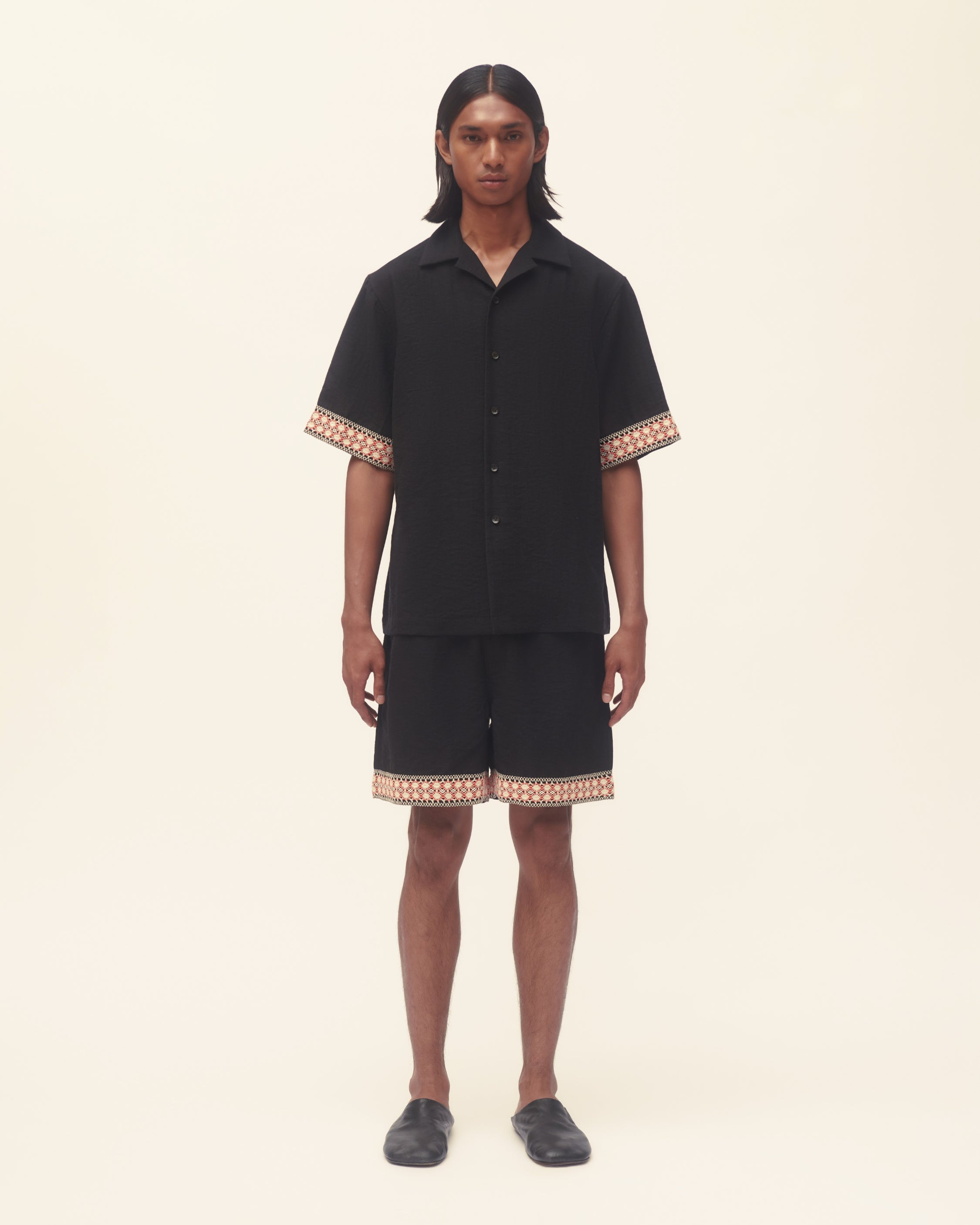 Person wearing a black outfit with patterned trim on a beige background