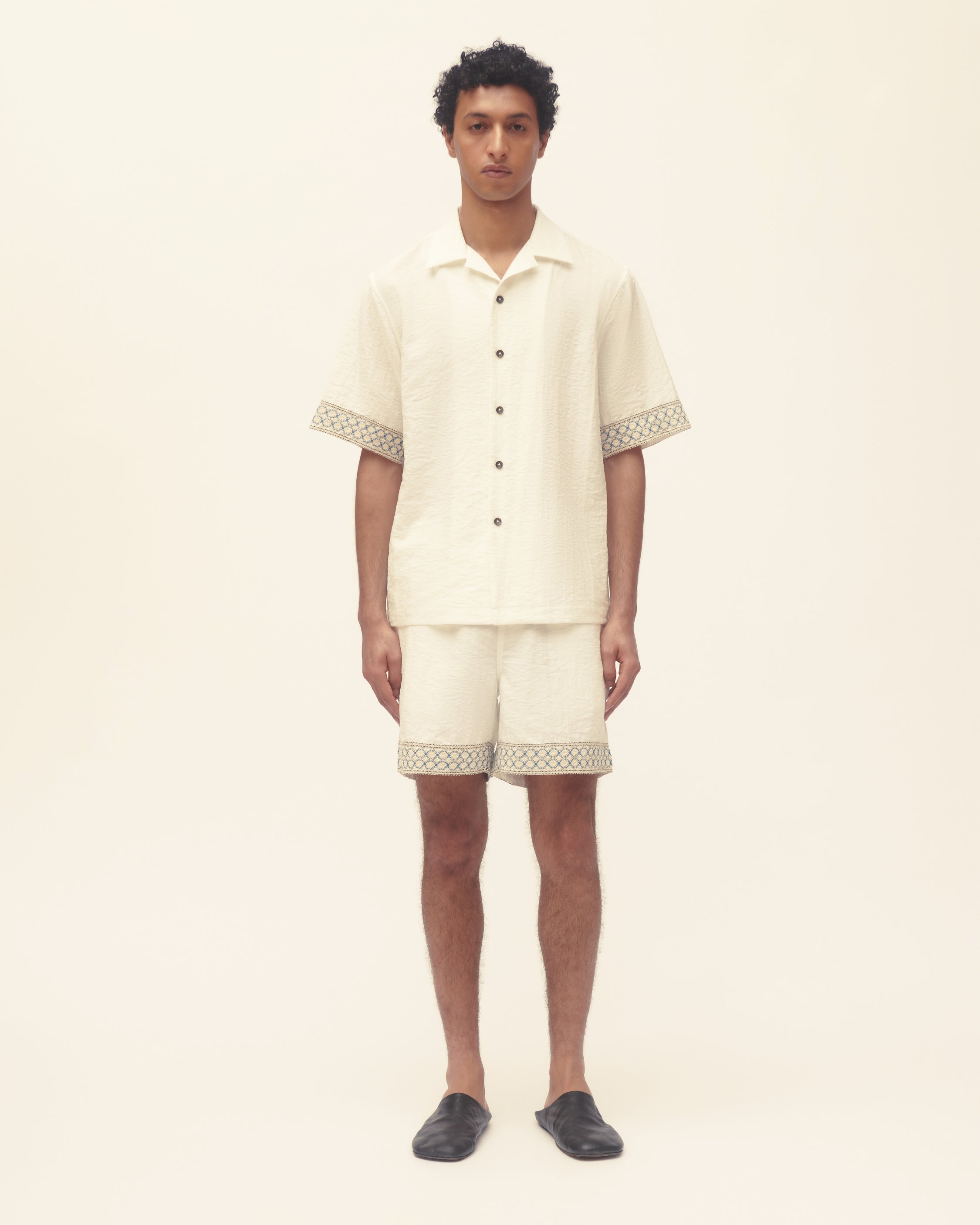 Man wearing a cream-colored outfit with patterned trim on a beige background