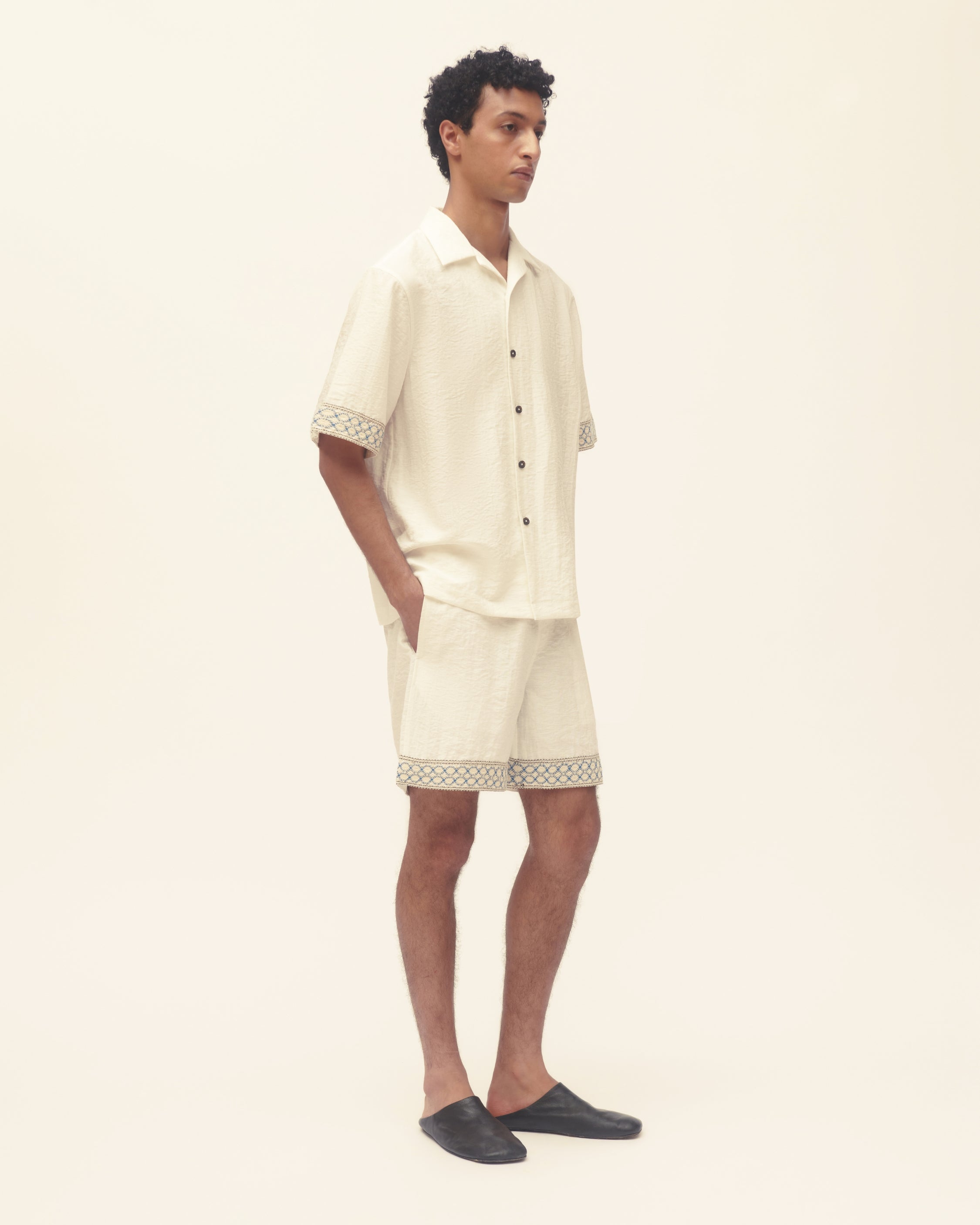 Person wearing a cream-colored outfit with black shoes on a white background