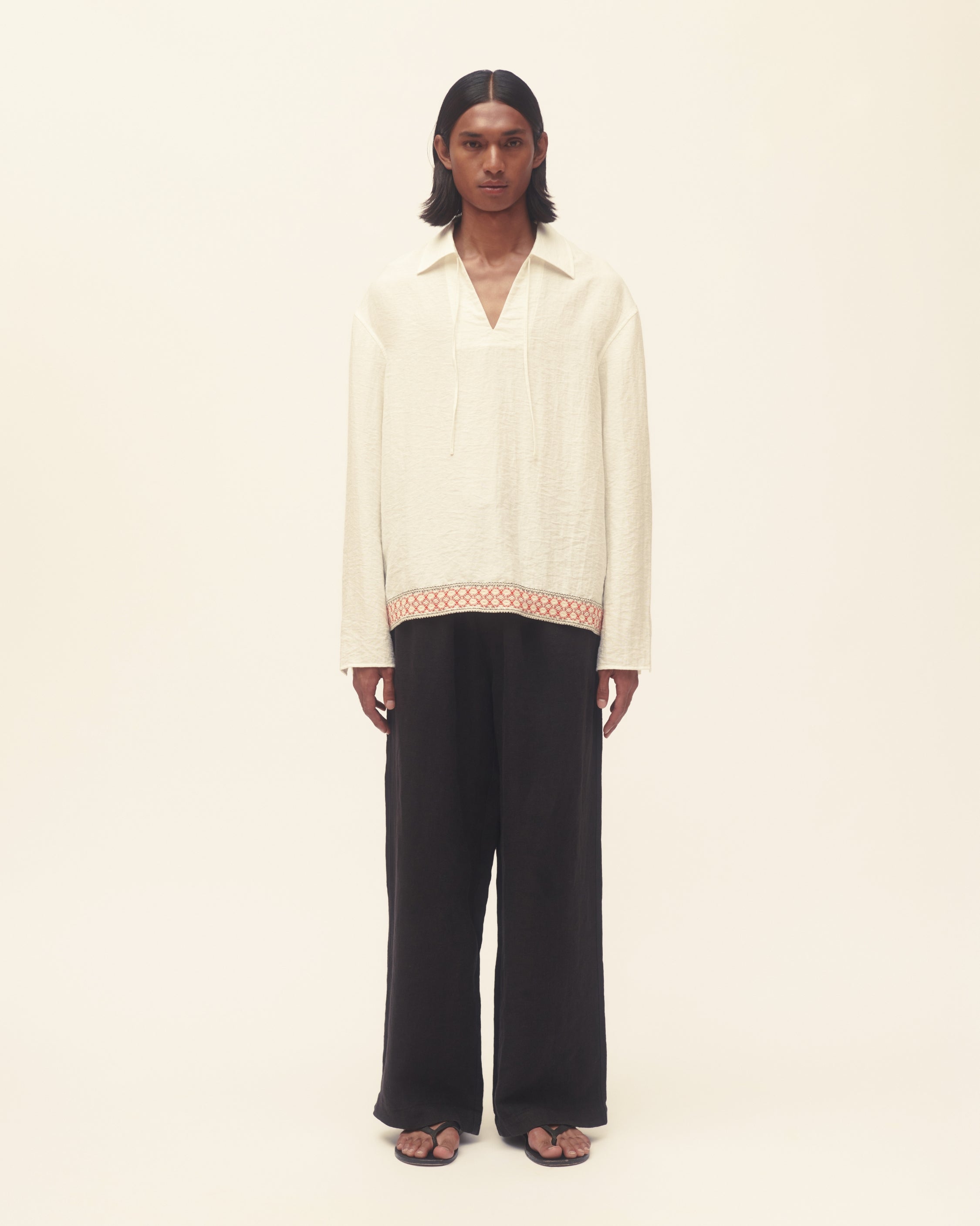 Person wearing a white long sleeve shirt and black pants on cream background