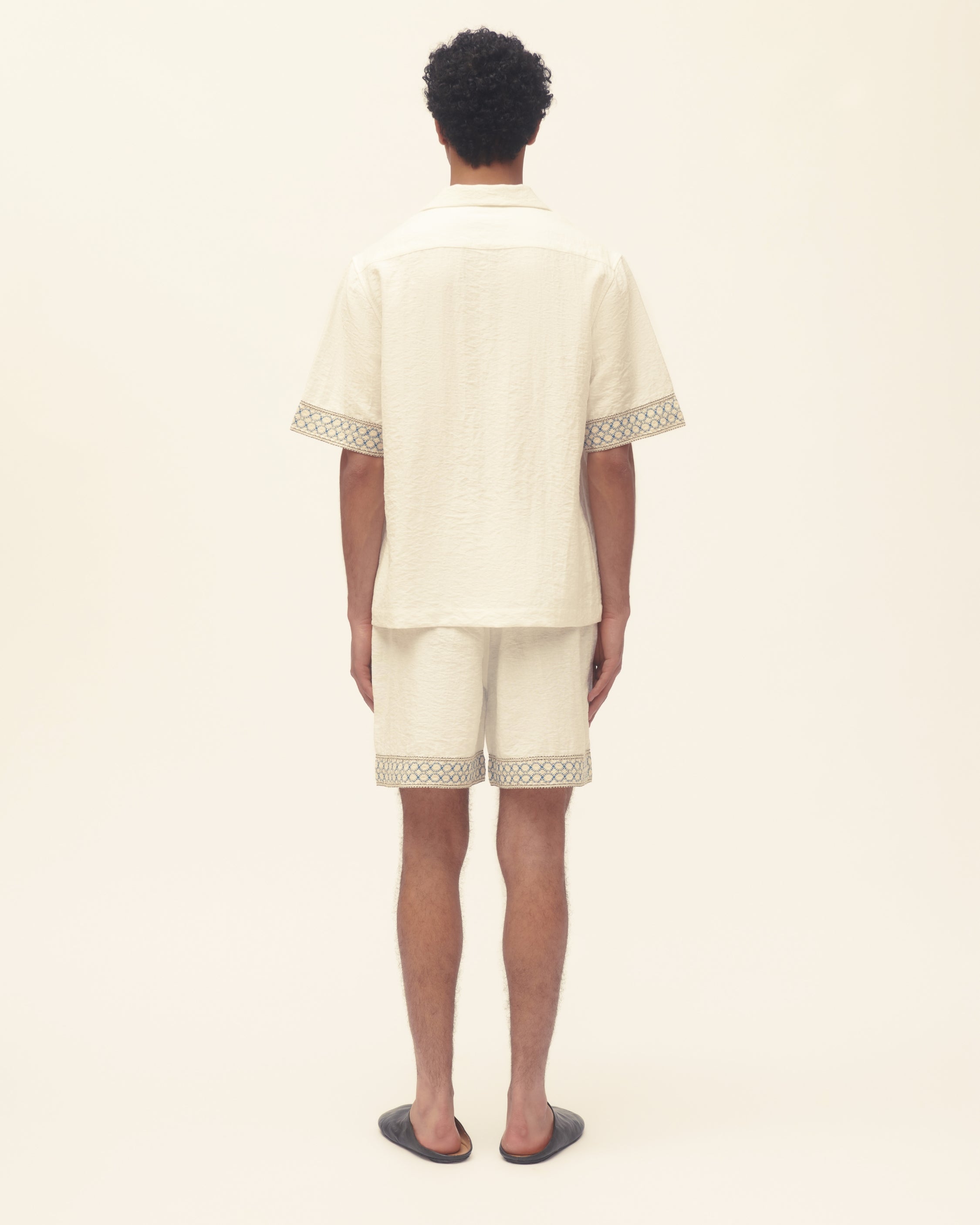 Person wearing a cream-colored outfit with lace trim on a white background