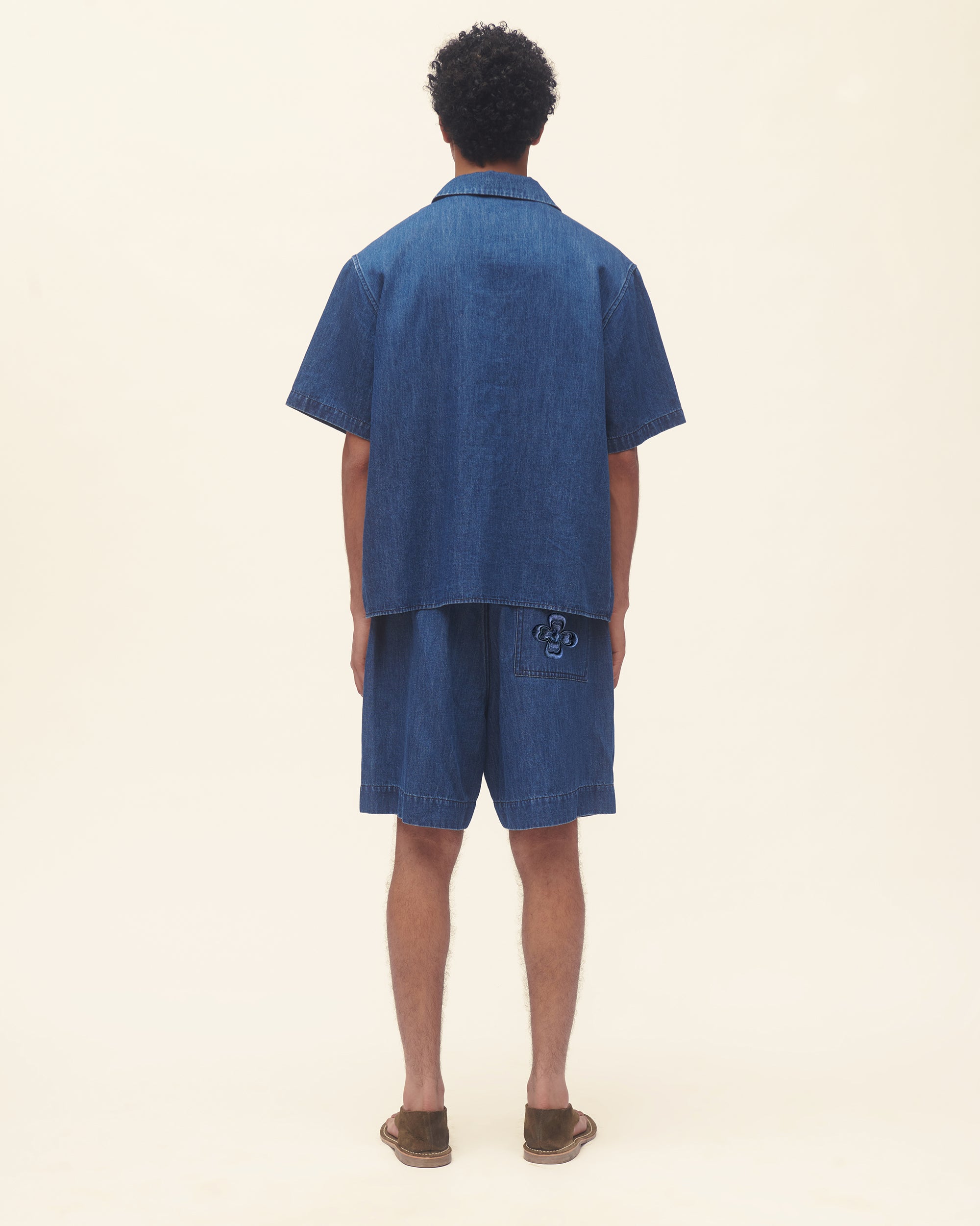 Man wearing a blue denim shirt and shorts on a beige background