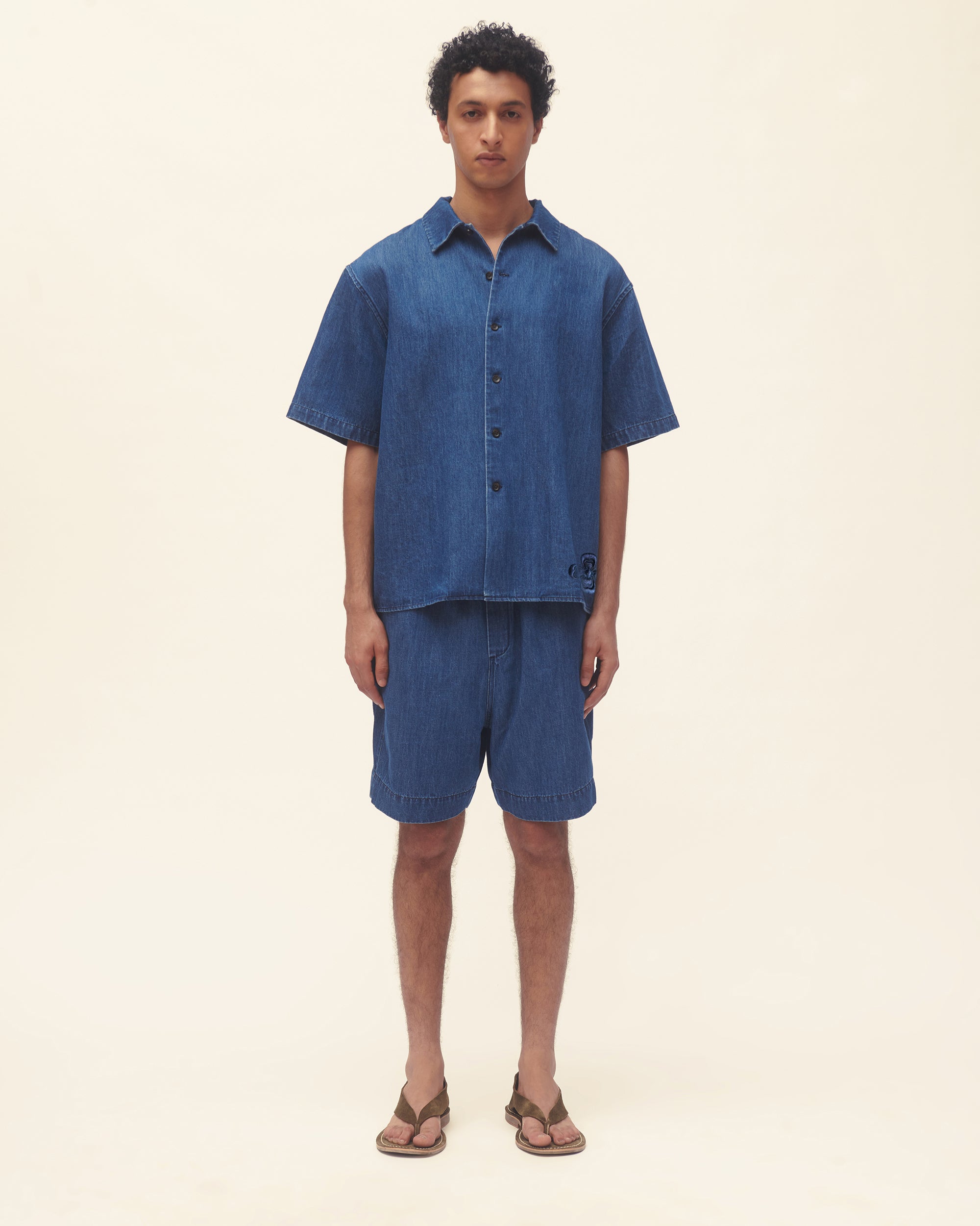 Man wearing a blue shirt and shorts set on a beige background