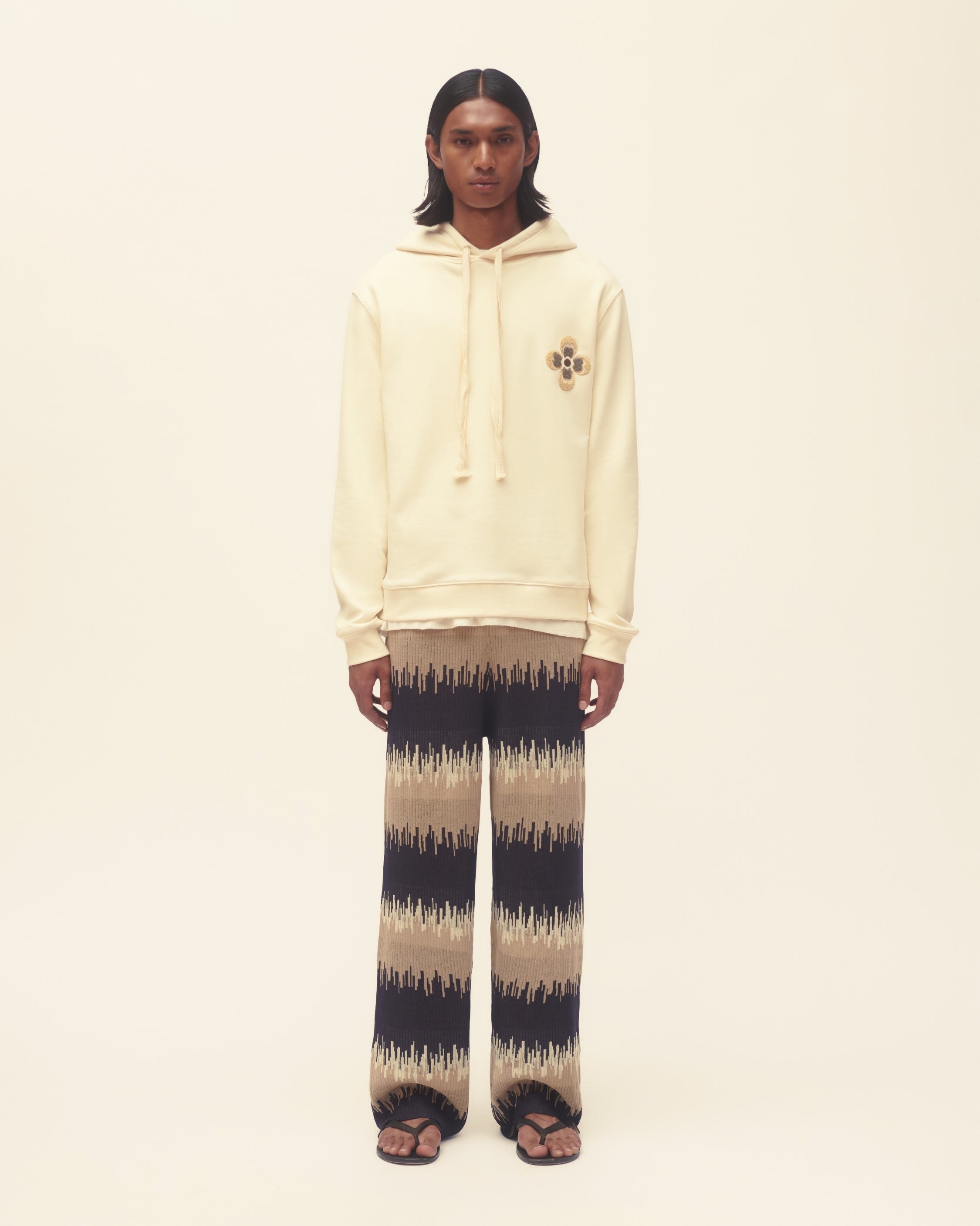 Person wearing a beige hoodie and wavy print pants on a plain background