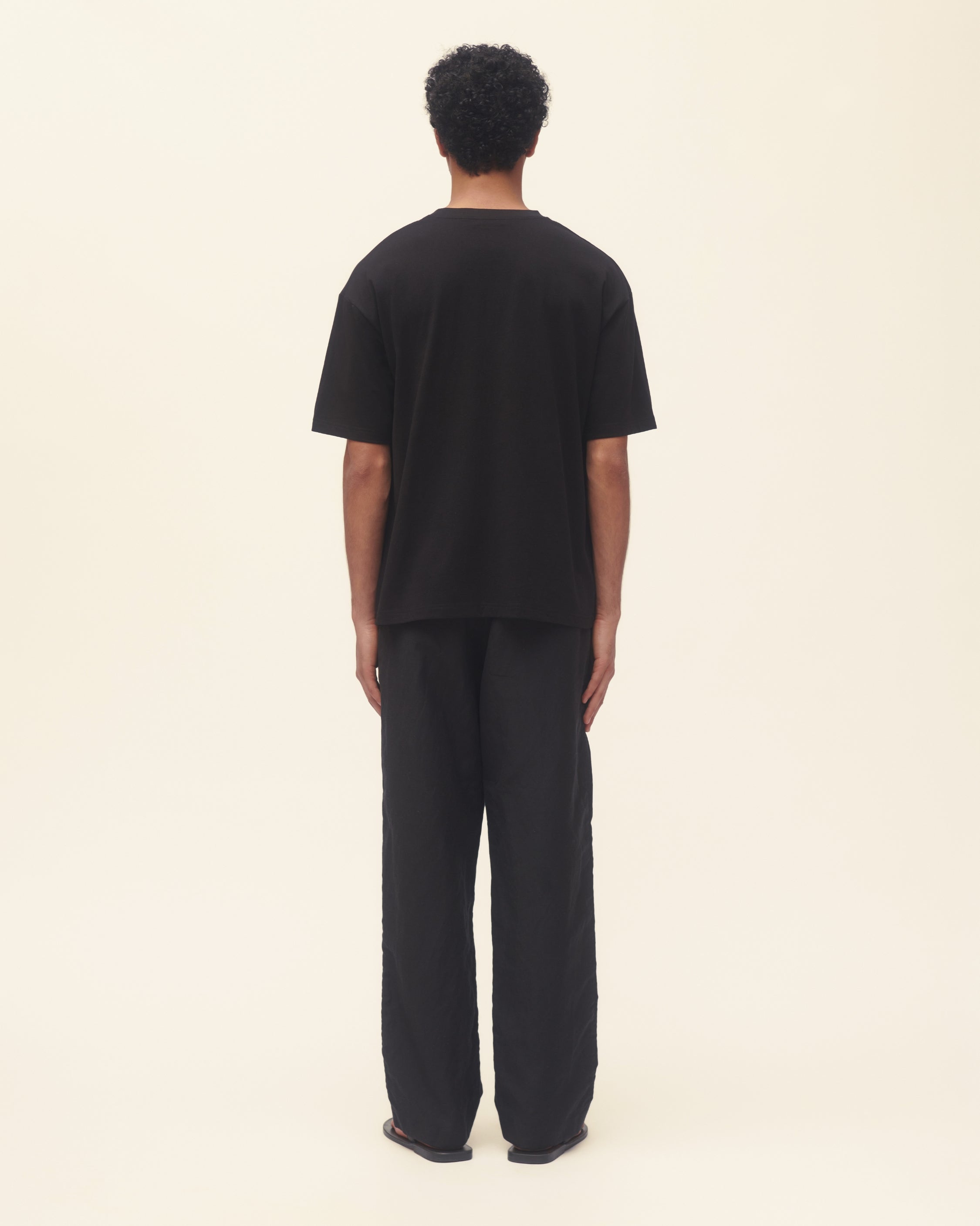 Person wearing a black t-shirt with a blue flower design and black pants on a beige background