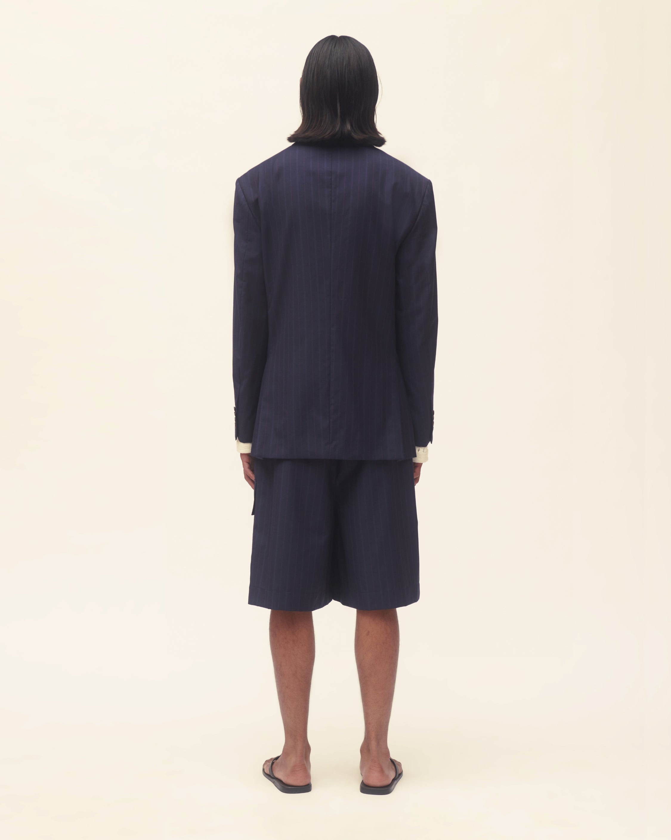 Person wearing a navy blue jacket over a white shirt on a beige background