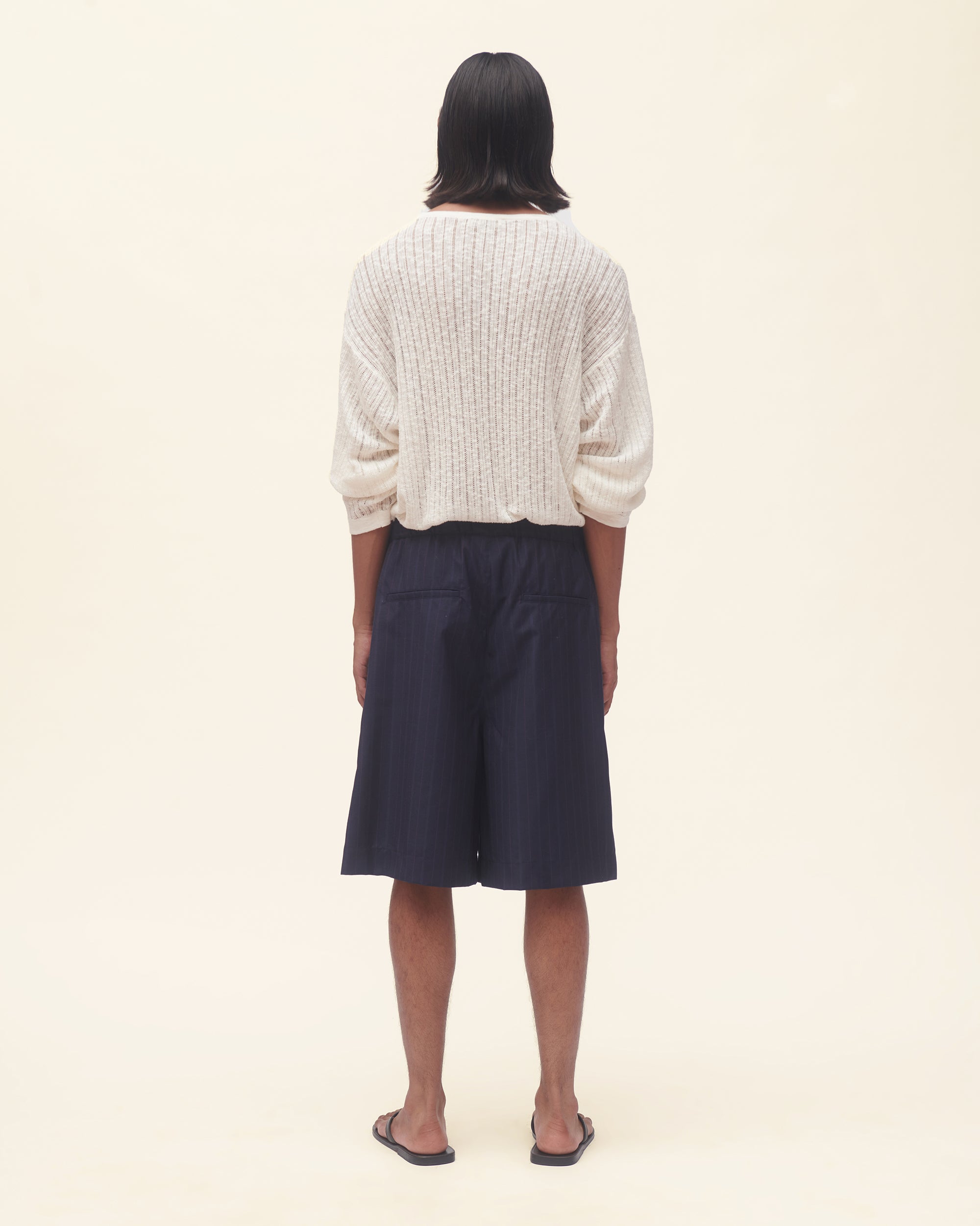 Person wearing a white ribbed sweater and navy shorts on a beige background