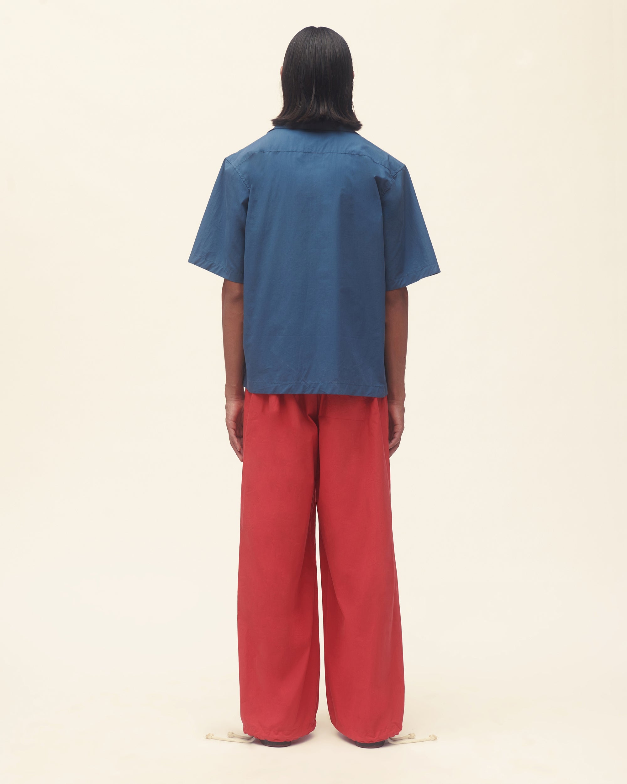 Person wearing a blue shirt with red floral patterns and red pants on a beige background