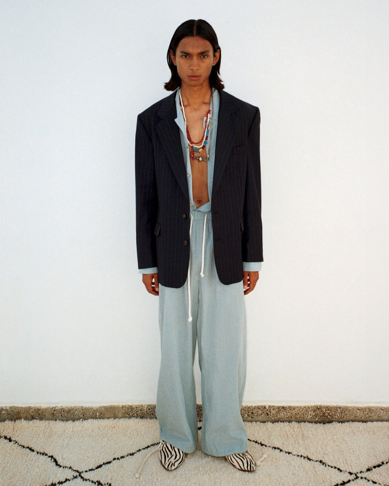 Person wearing a dark blazer and light pants standing on a patterned rug.