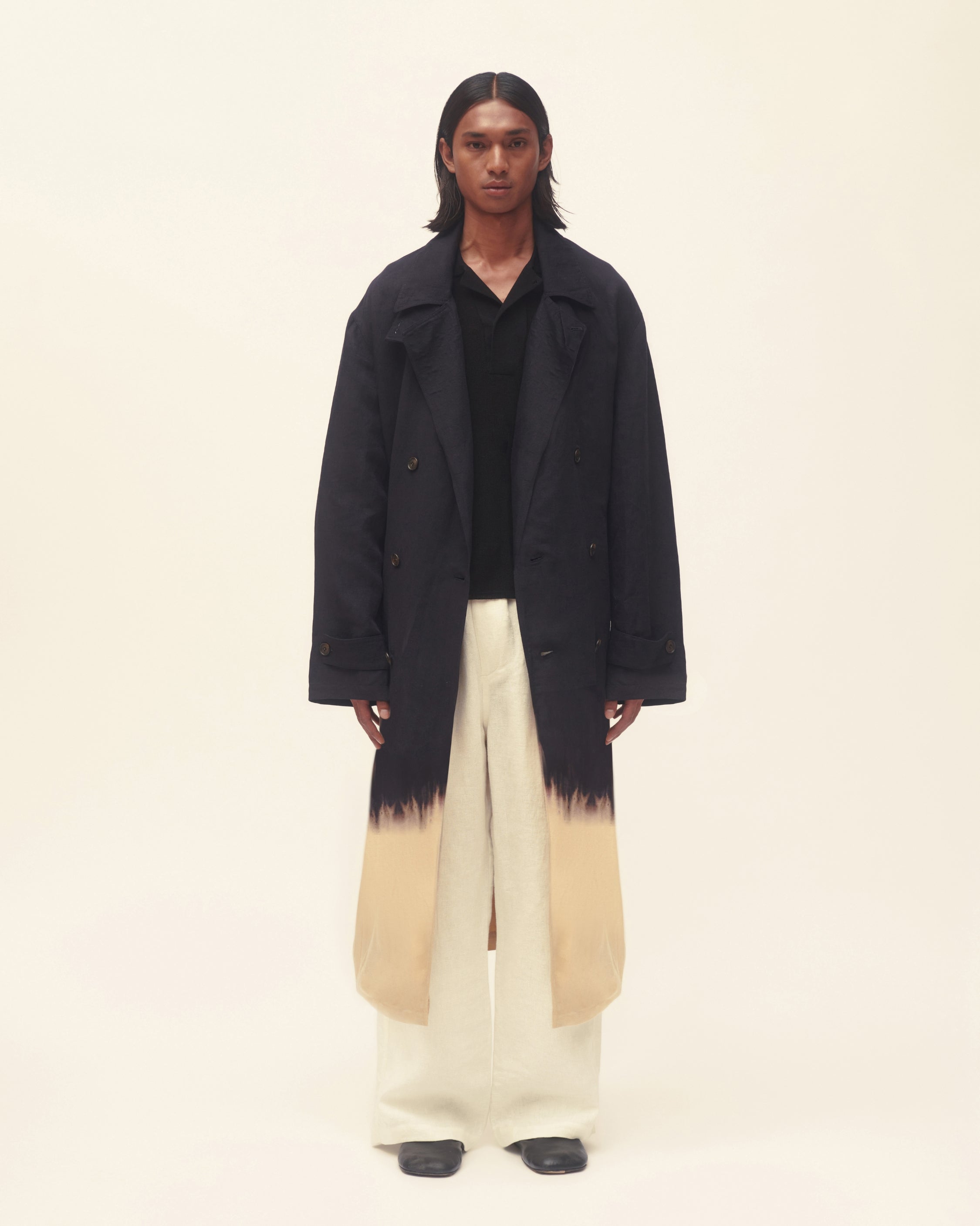 Person wearing a black coat with a gradient design, standing against a plain background