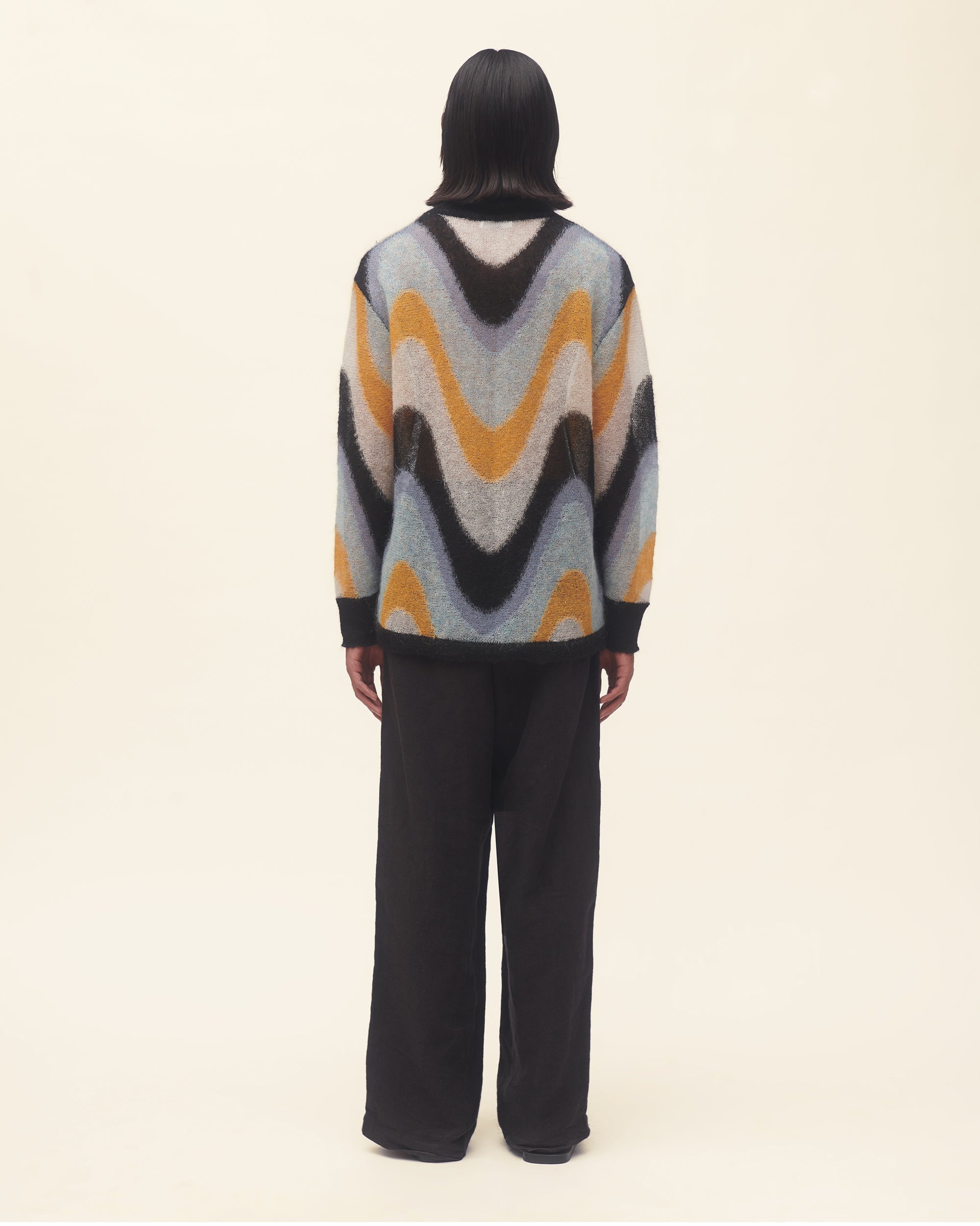 Person wearing a colorful sweater with wavy pattern on a beige background