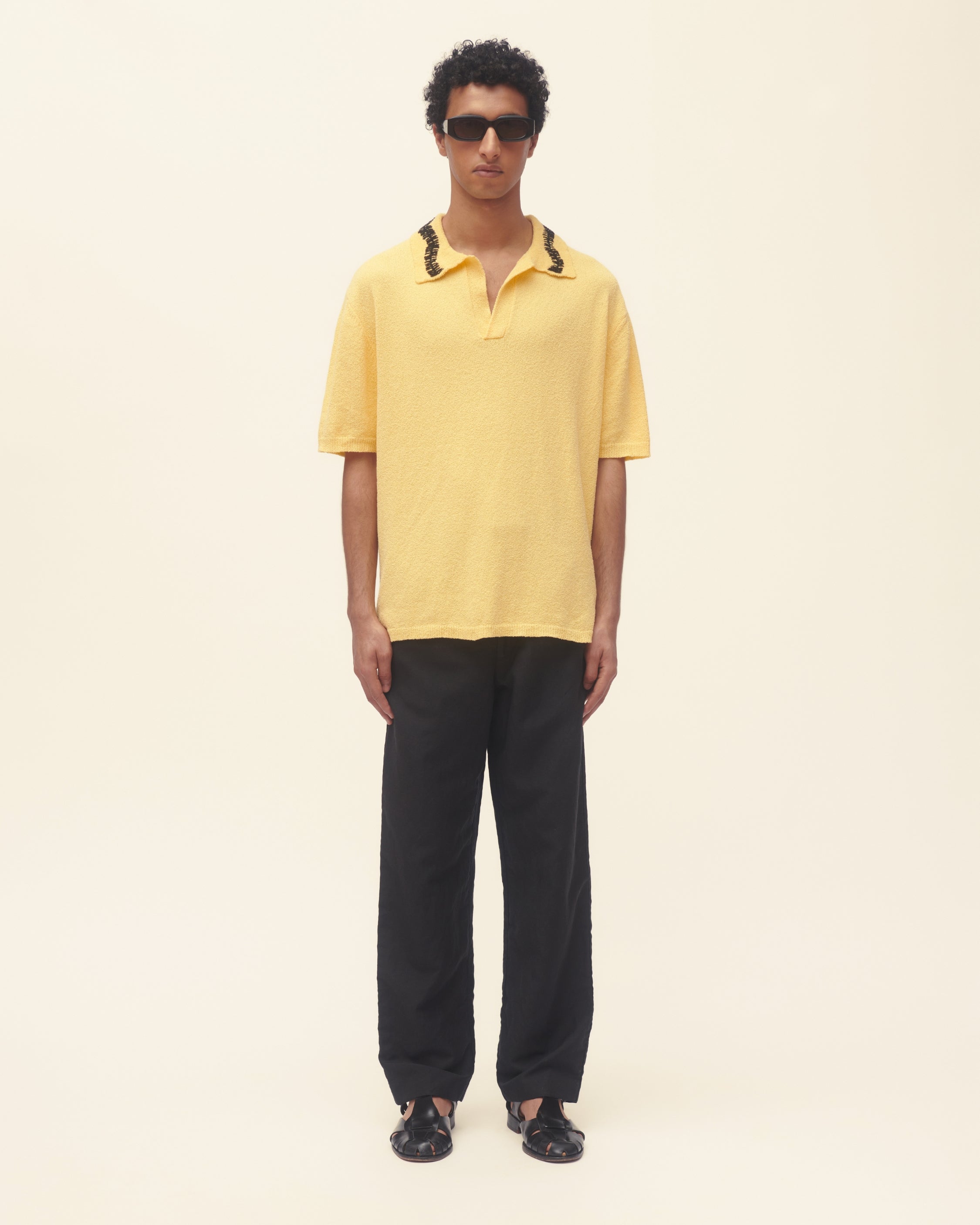 Man wearing a yellow polo shirt and black pants on a beige background