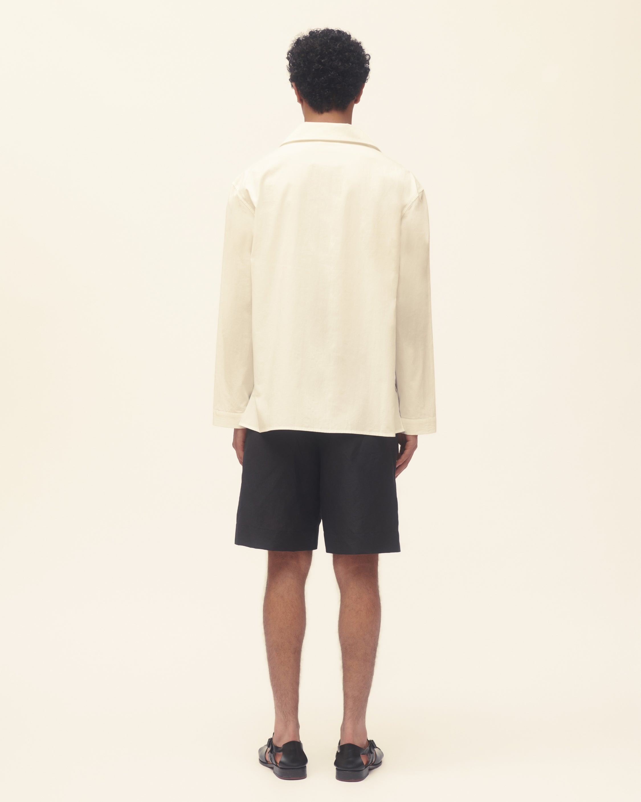 Man wearing a cream shirt and black shorts on a plain background