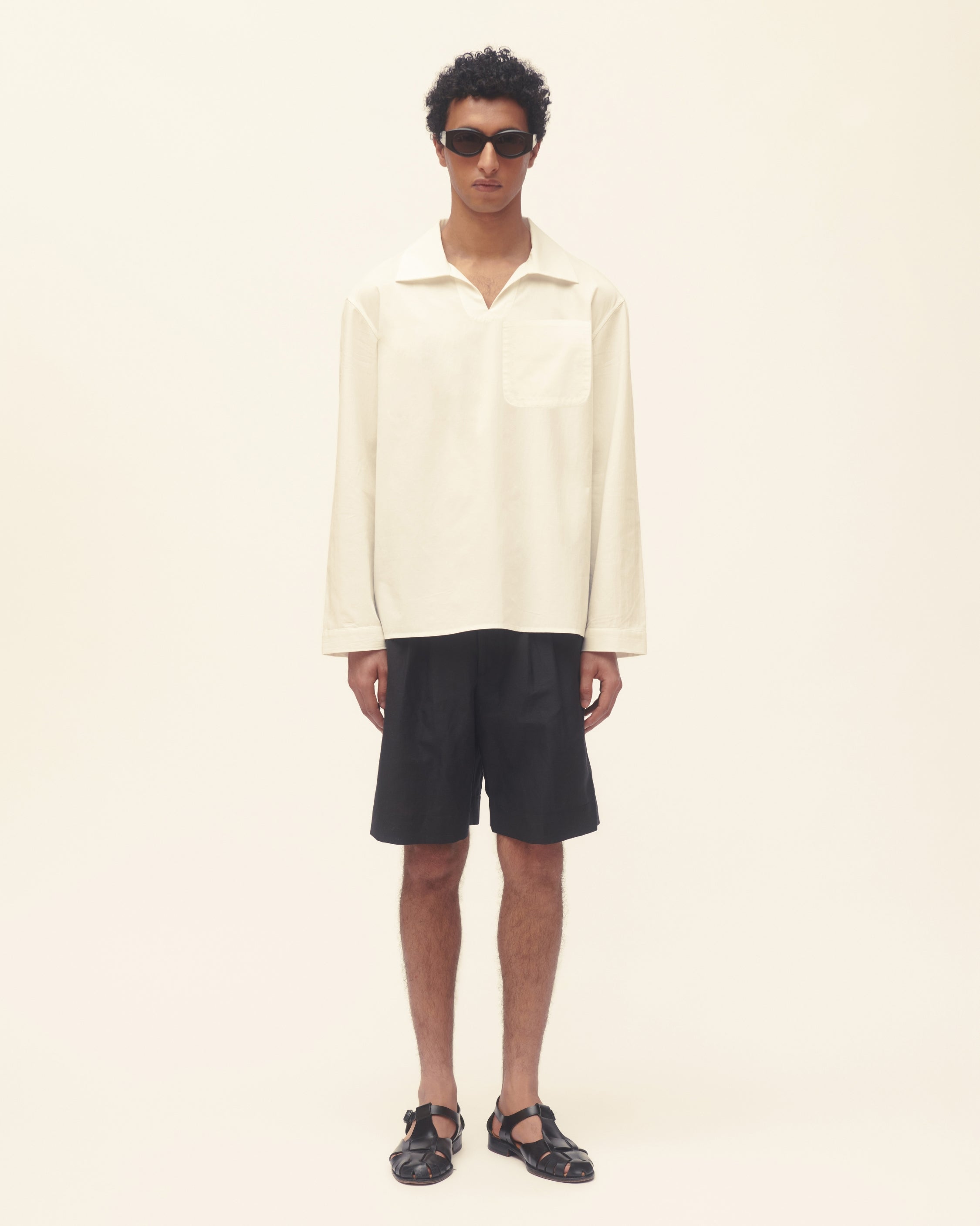 Man wearing a cream shirt and black shorts on a plain background