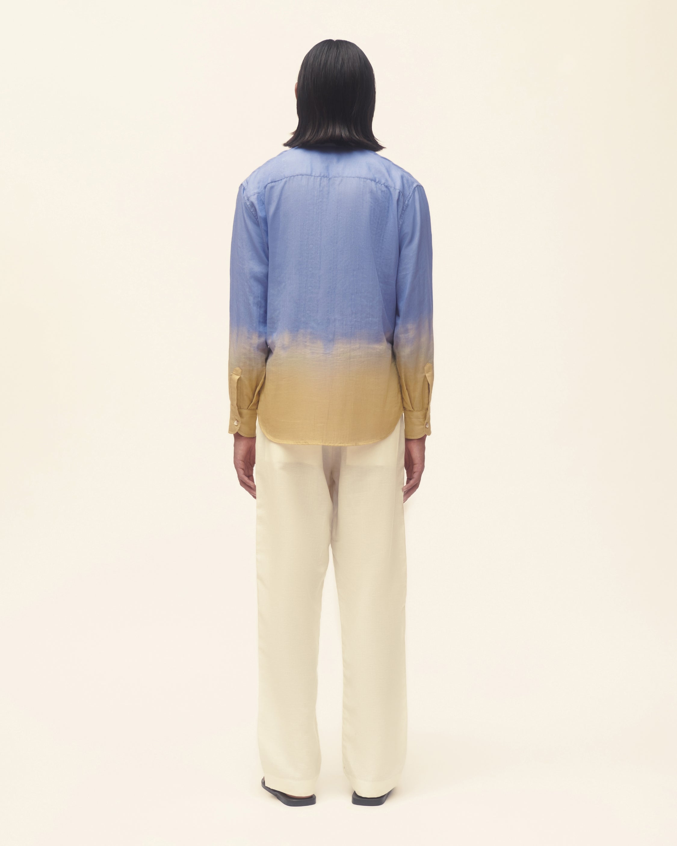 Person wearing a blue and yellow gradient shirt with beige pants on a white background