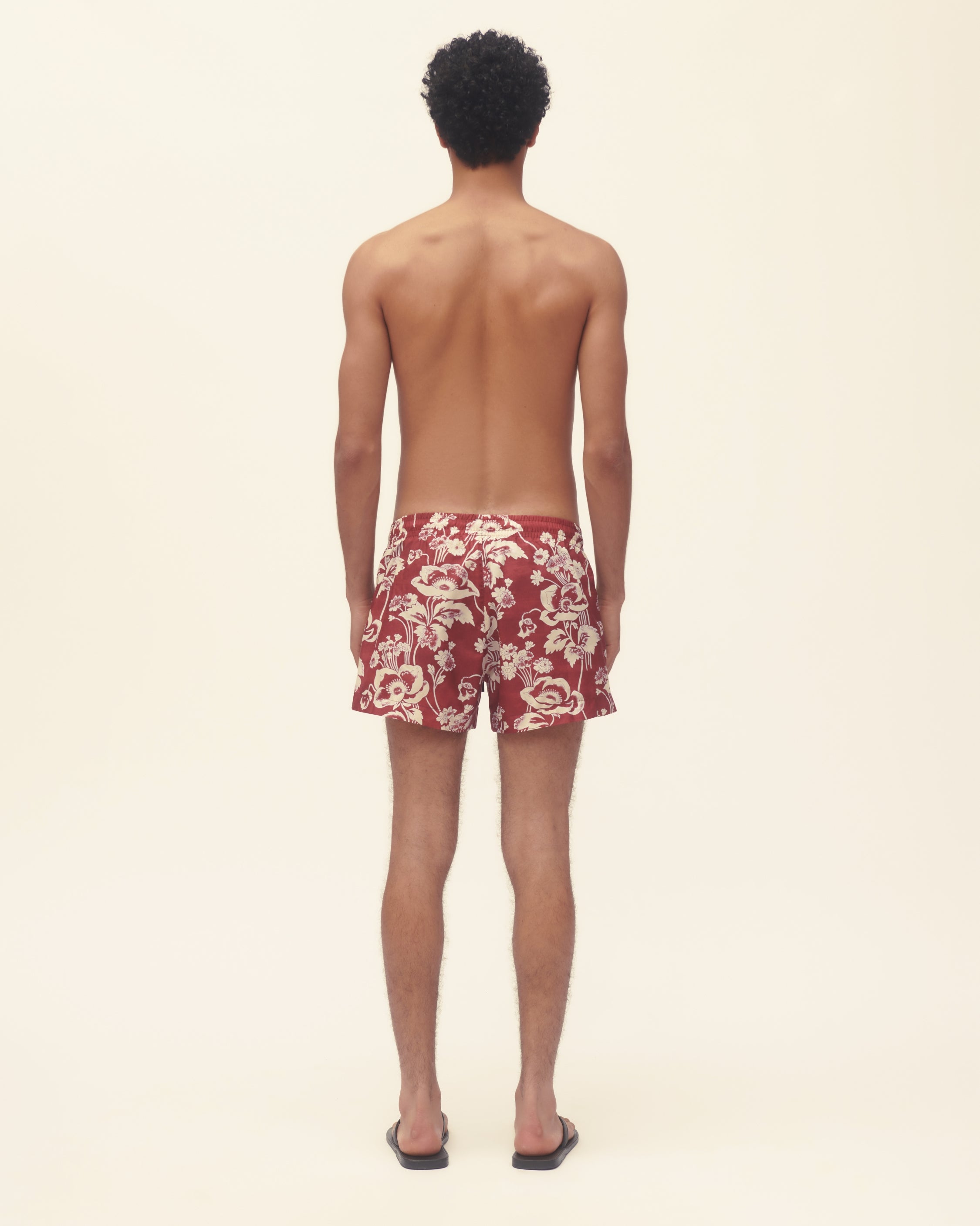 Person wearing red floral swim shorts on a beige background