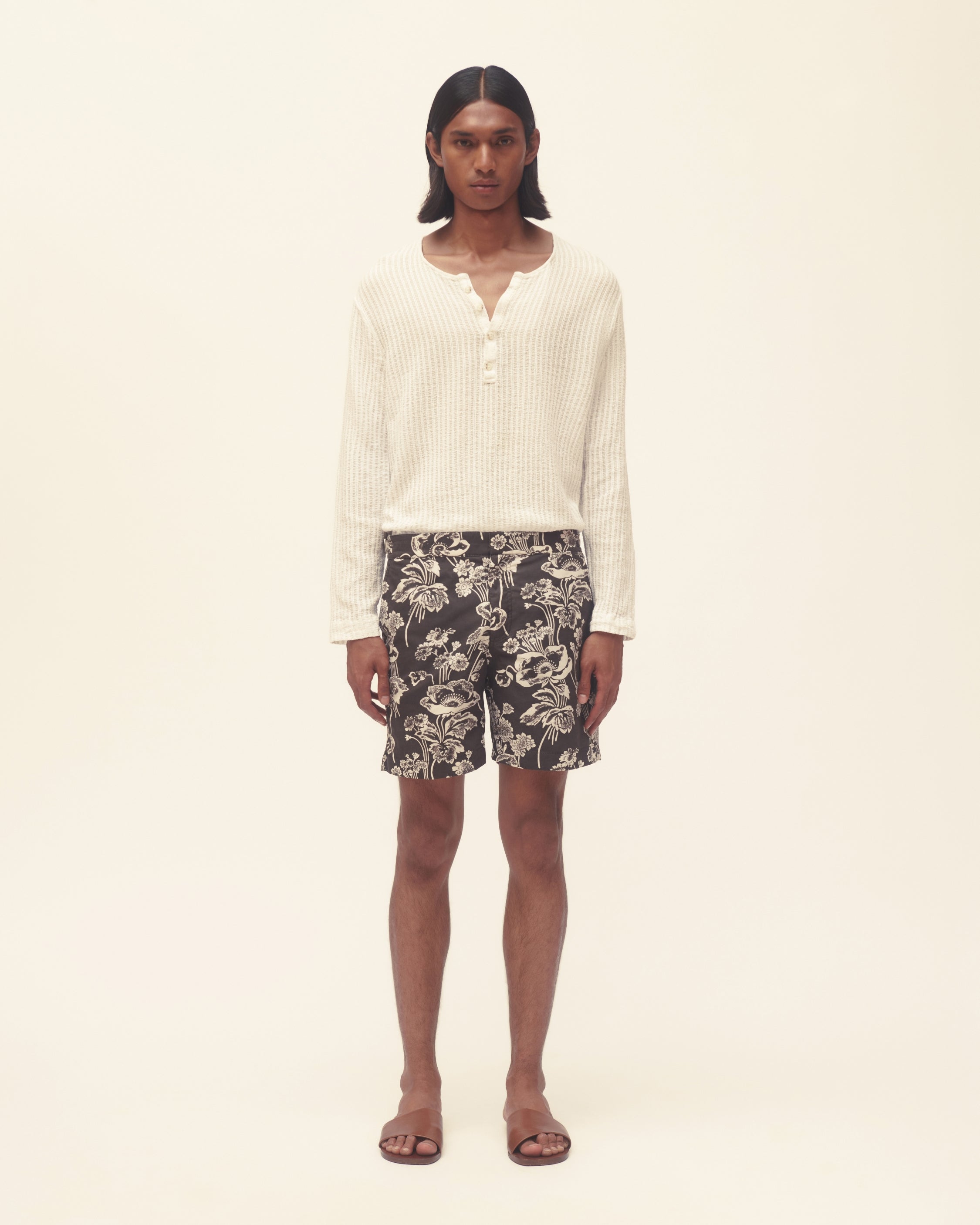 Person wearing patterned swim shorts with long sleeve white shirt on beige background