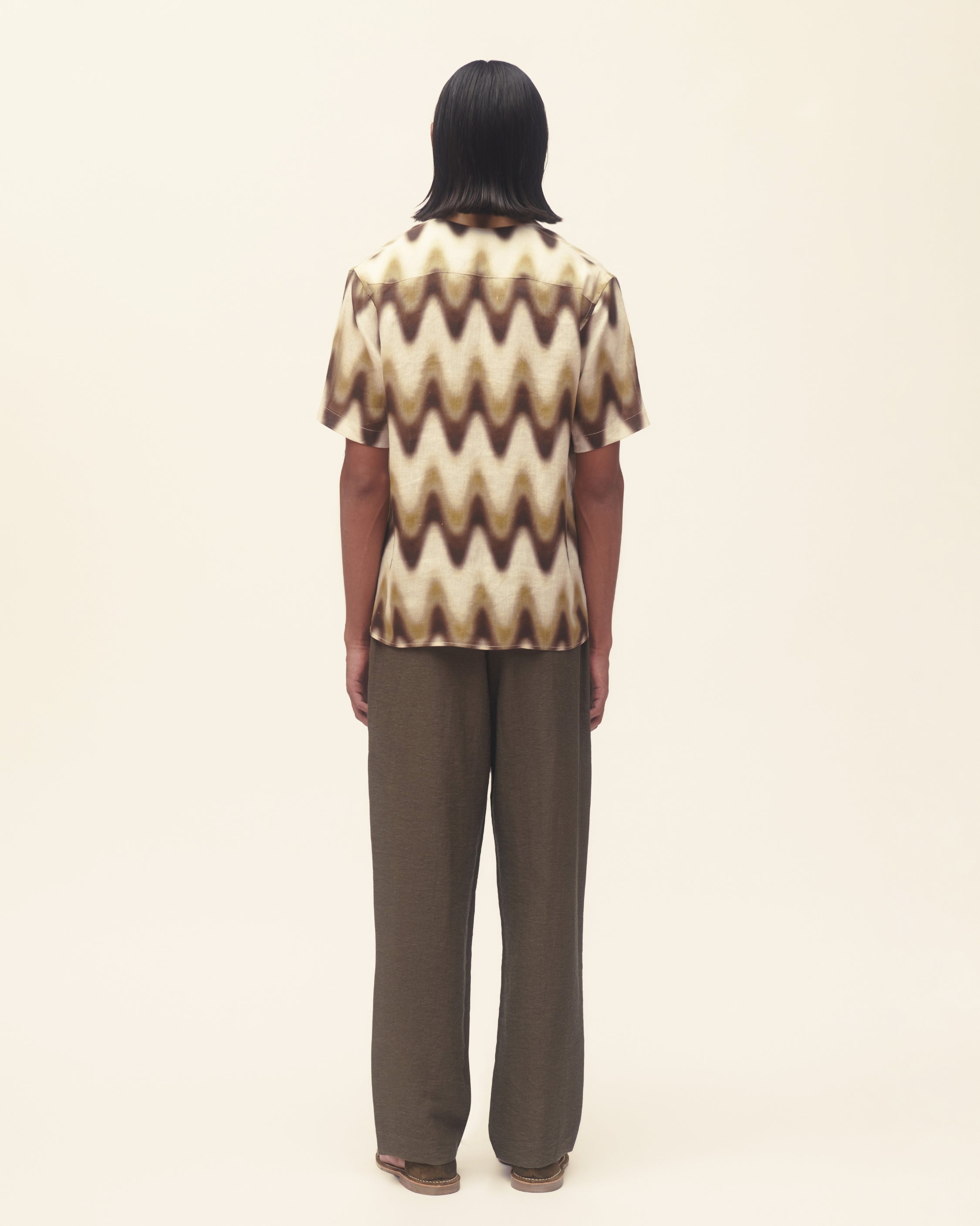 Person wearing a patterned shirt and brown pants on a plain background