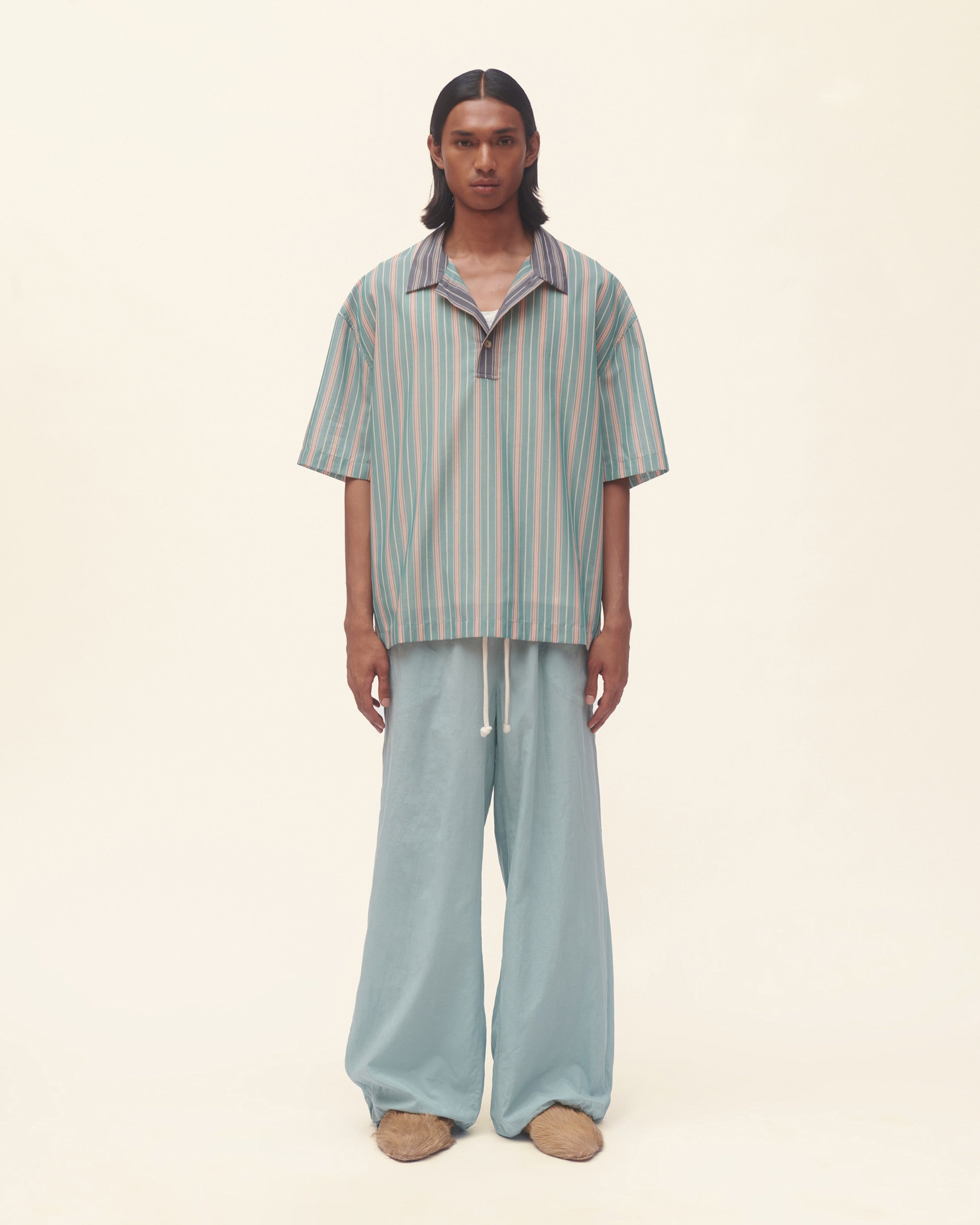 Person wearing a striped shirt and light blue pants on a beige background