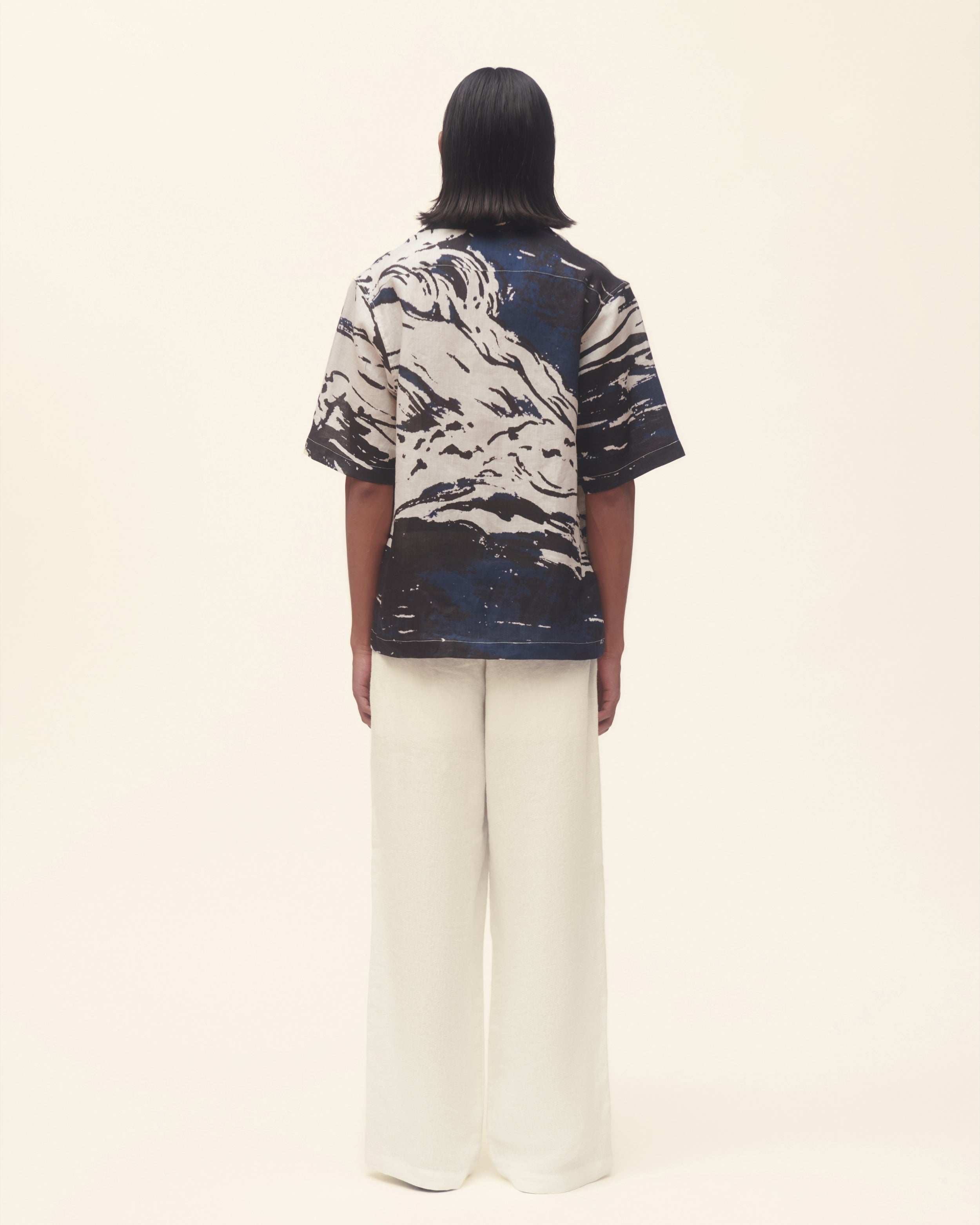 Person wearing a black and white printed shirt with wide-leg pants on a beige background