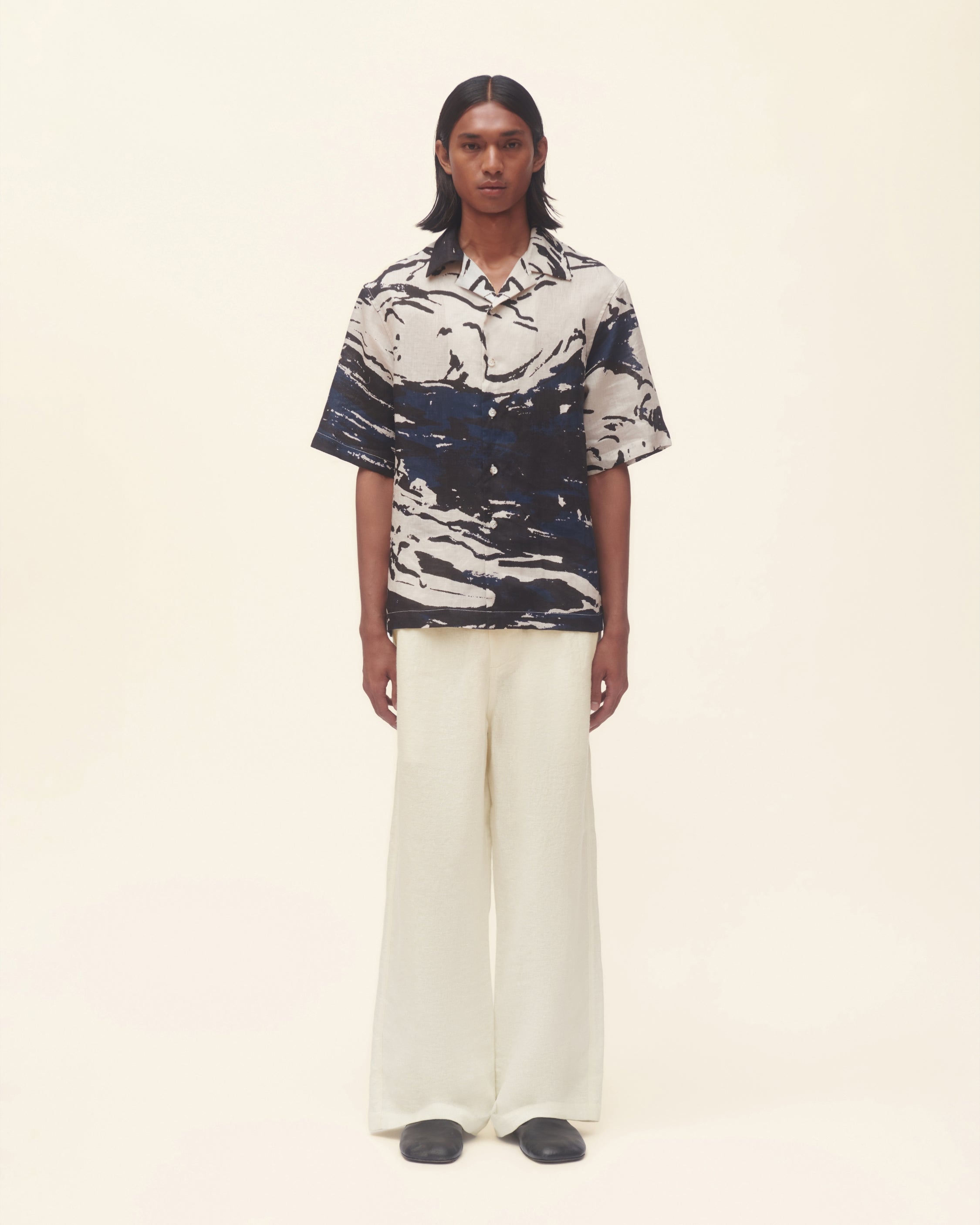 Person wearing a patterned shirt and white pants on a beige background