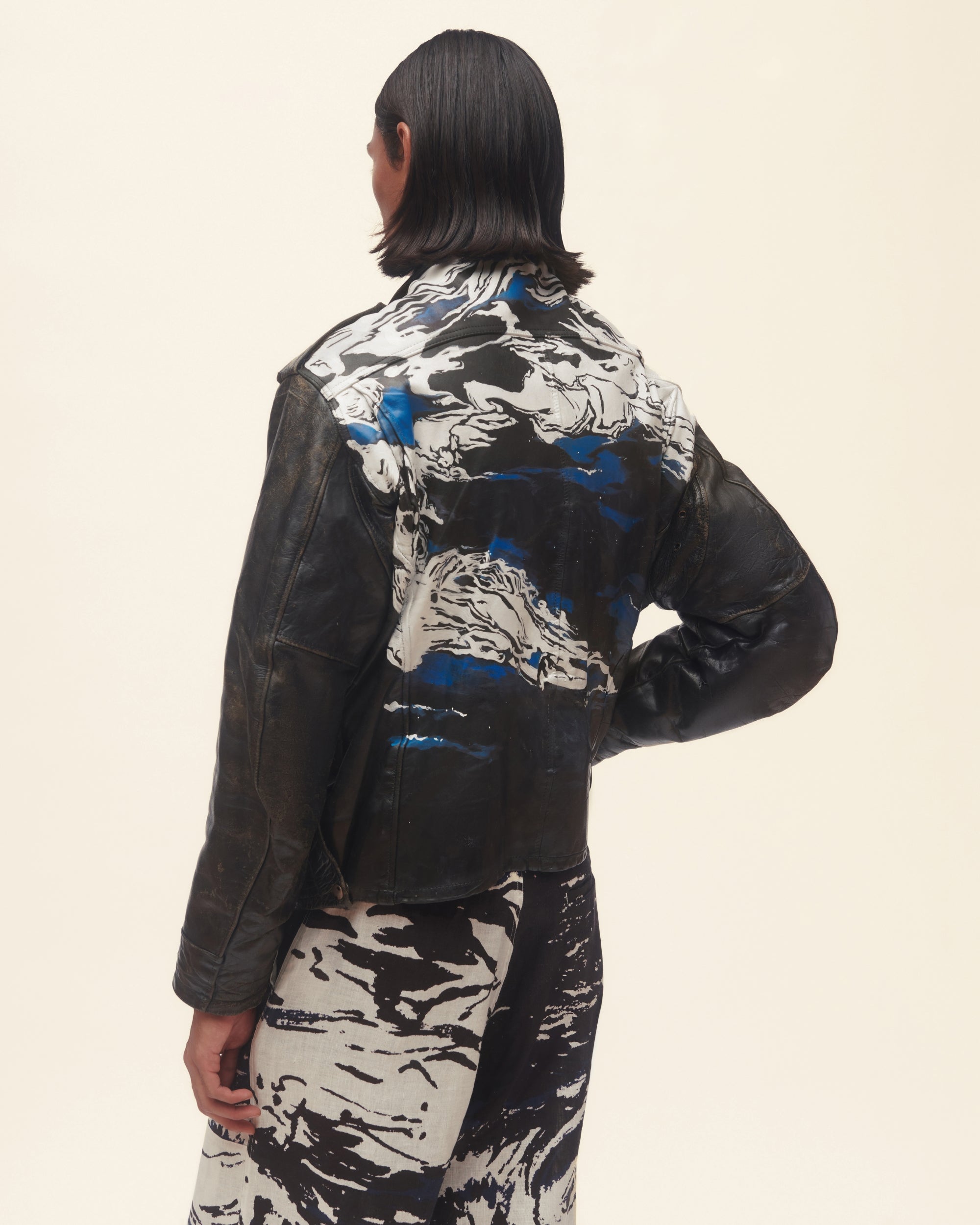 Person wearing a black leather jacket on a beige background