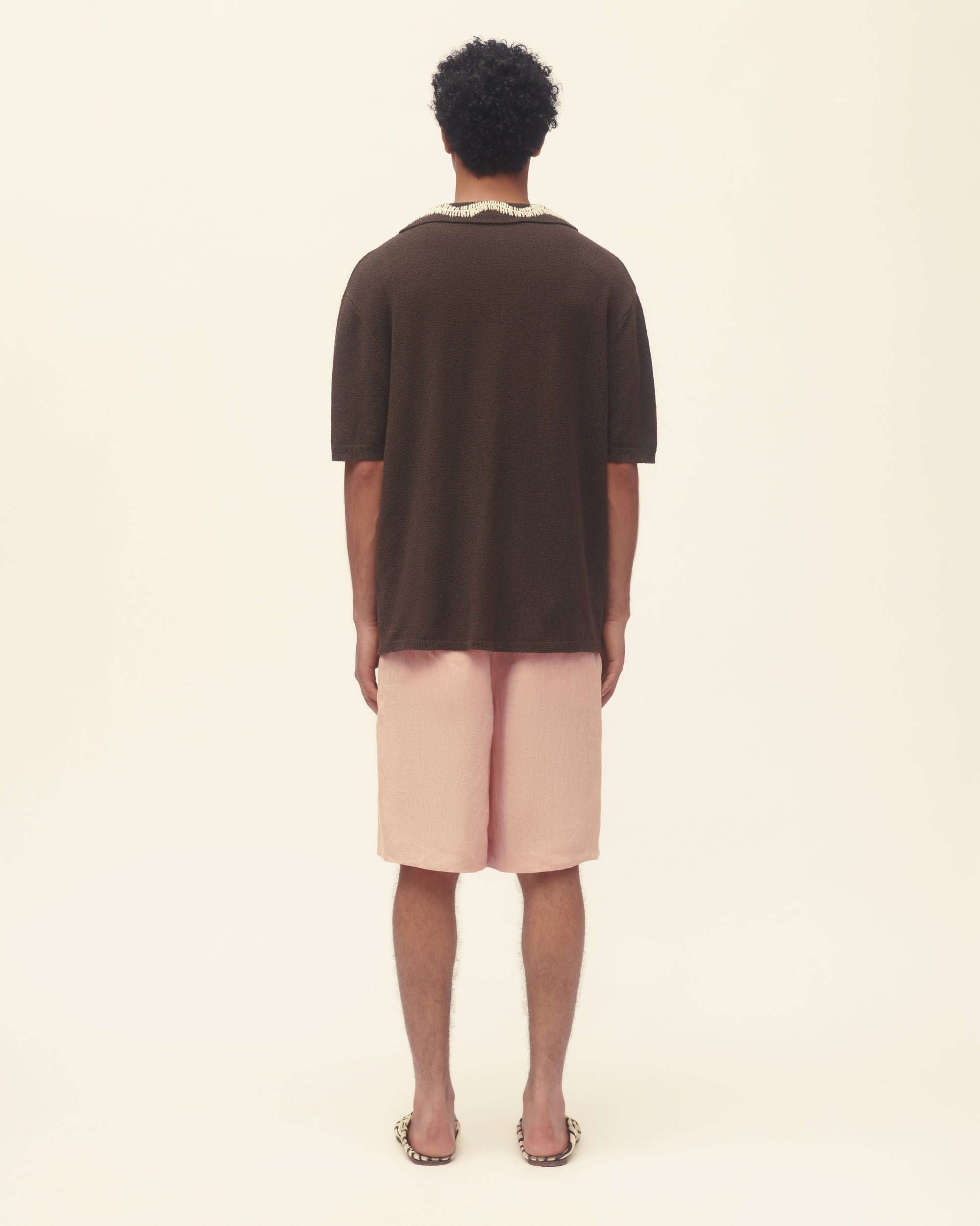 Person wearing a brown shirt and pink shorts on a beige background