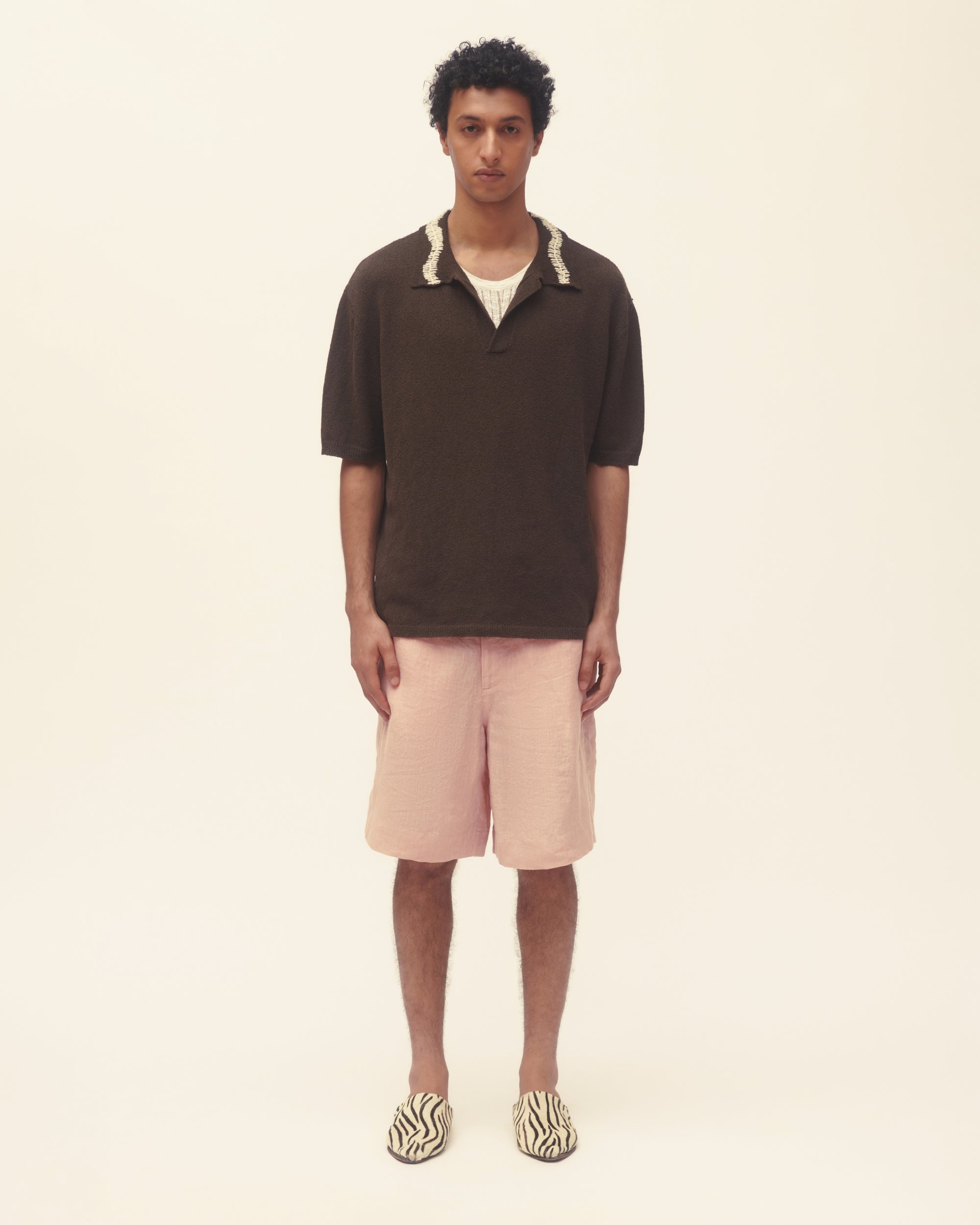 Person wearing a brown shirt and pink shorts on a beige background