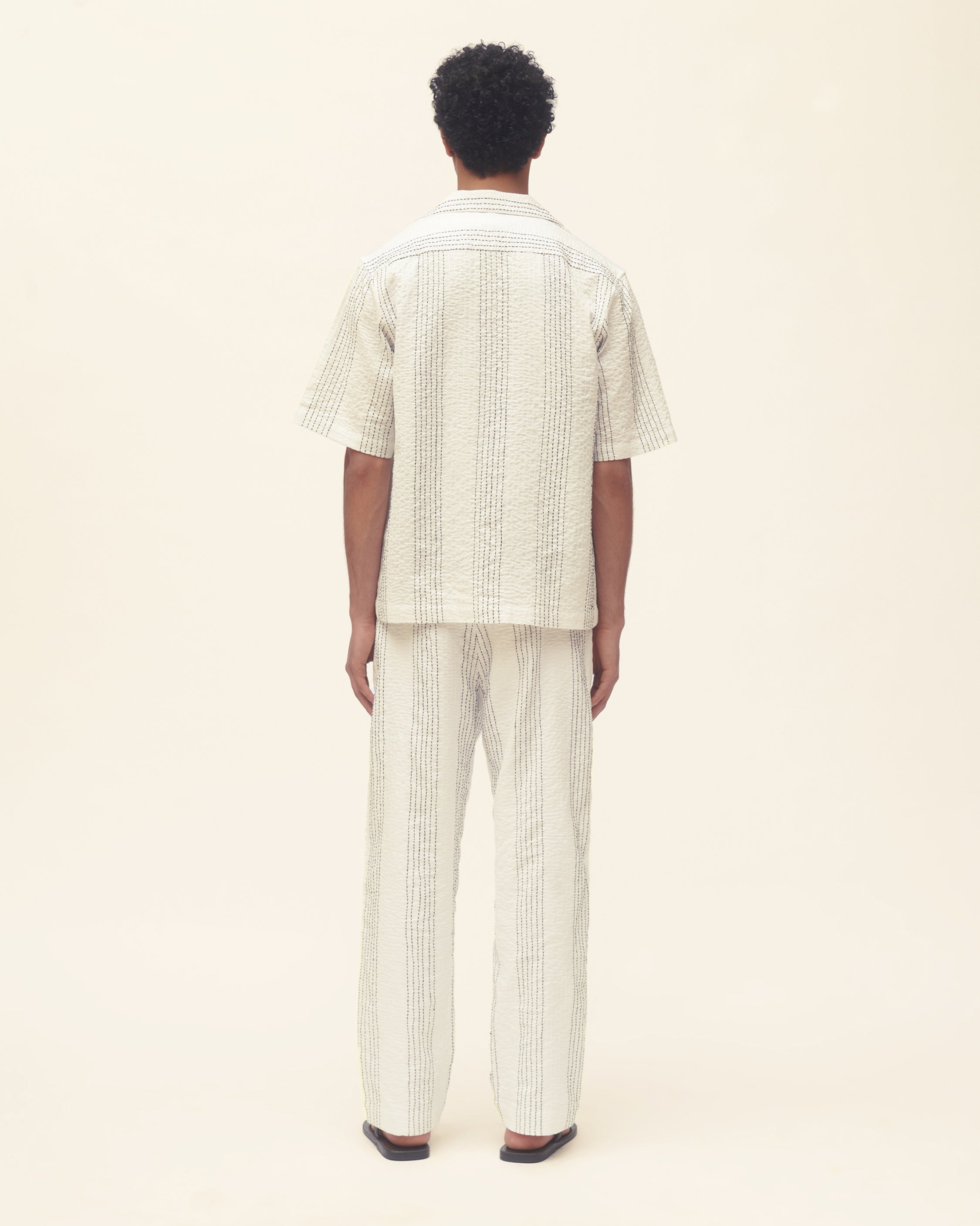 Person wearing a matching striped shirt and pants set on a beige background