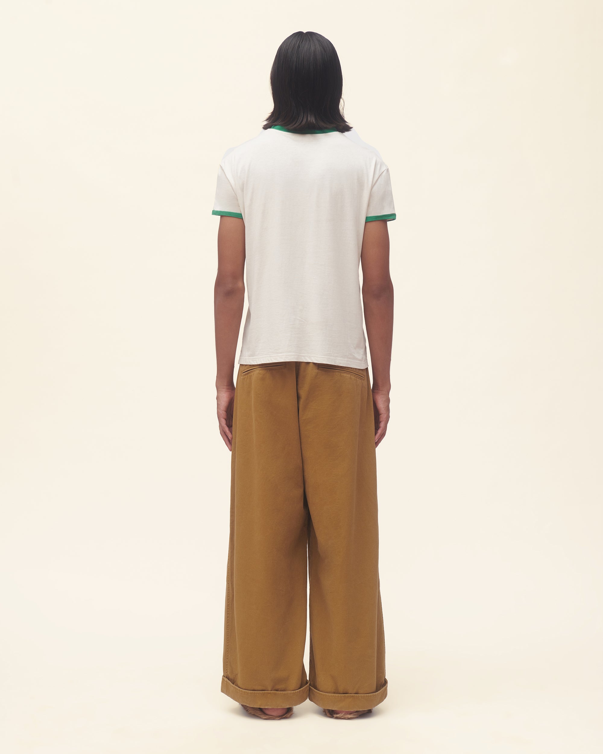 Person wearing a white t-shirt with green text and graphics, paired with brown pants on a beige background