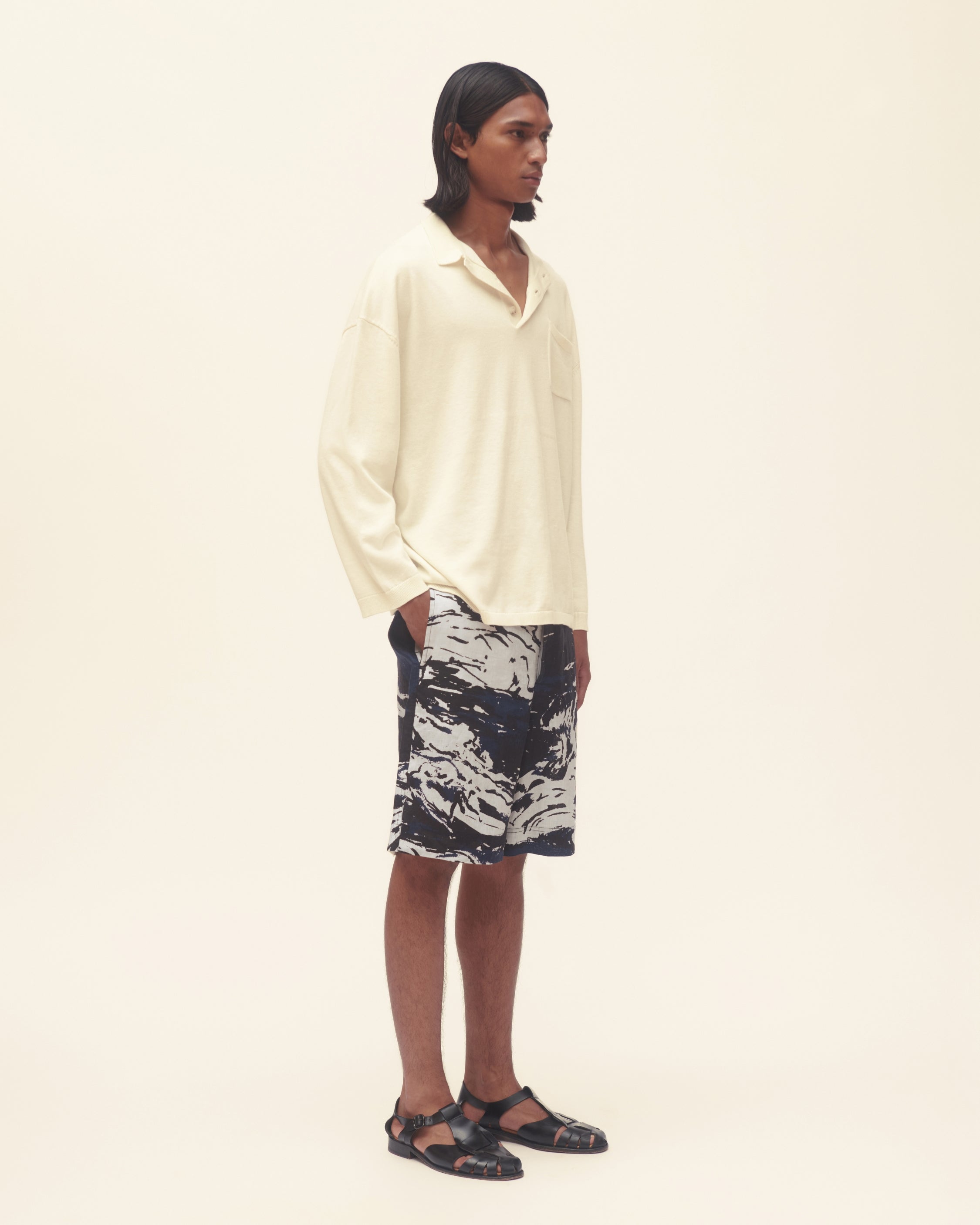 Person wearing a cream long-sleeve shirt and patterned shorts on a beige background