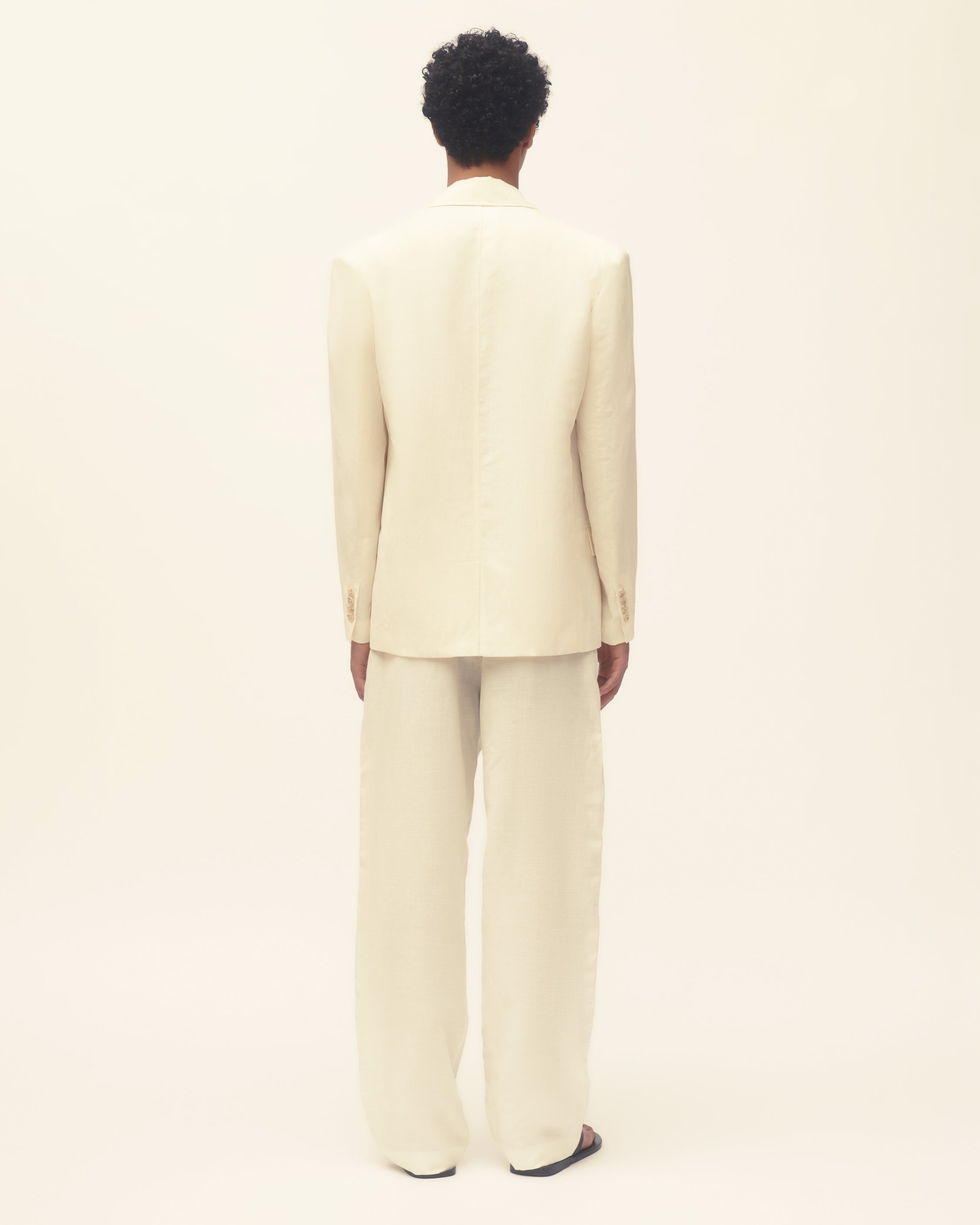 Person wearing a beige suit standing against a plain background