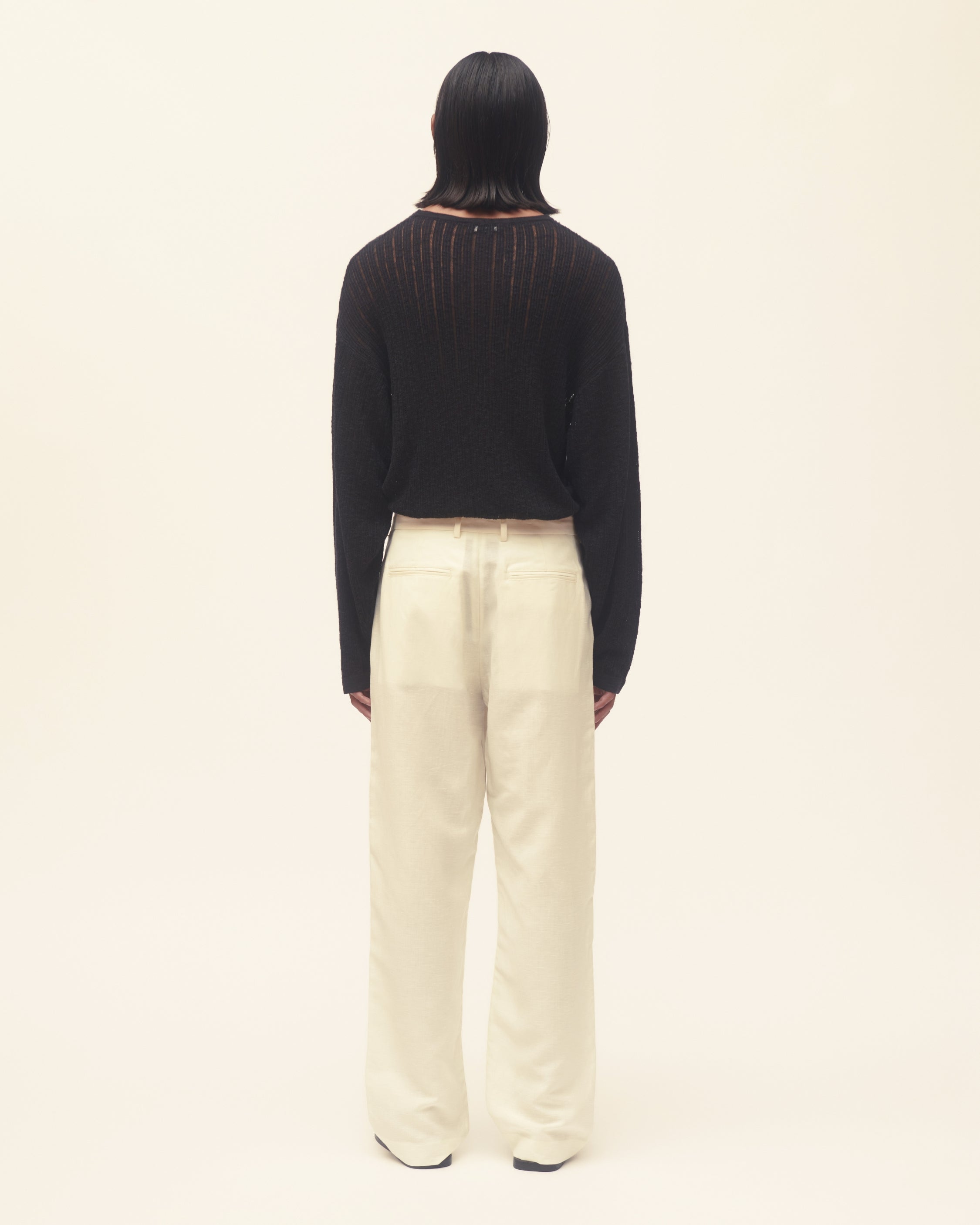 Person wearing a black sweater and off white pants on a white background