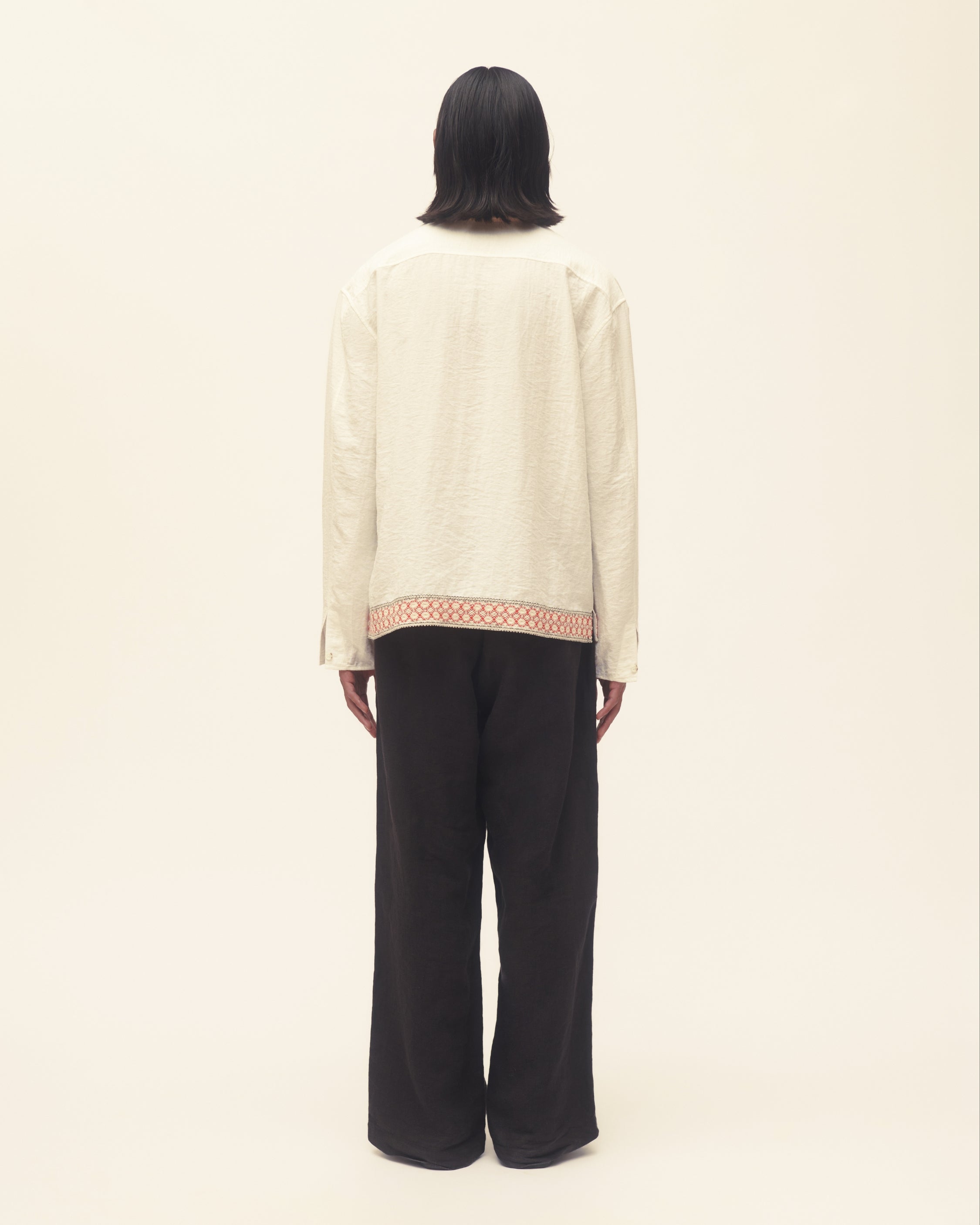 Person wearing a cream blouse with a patterned hem and black pants on a beige background