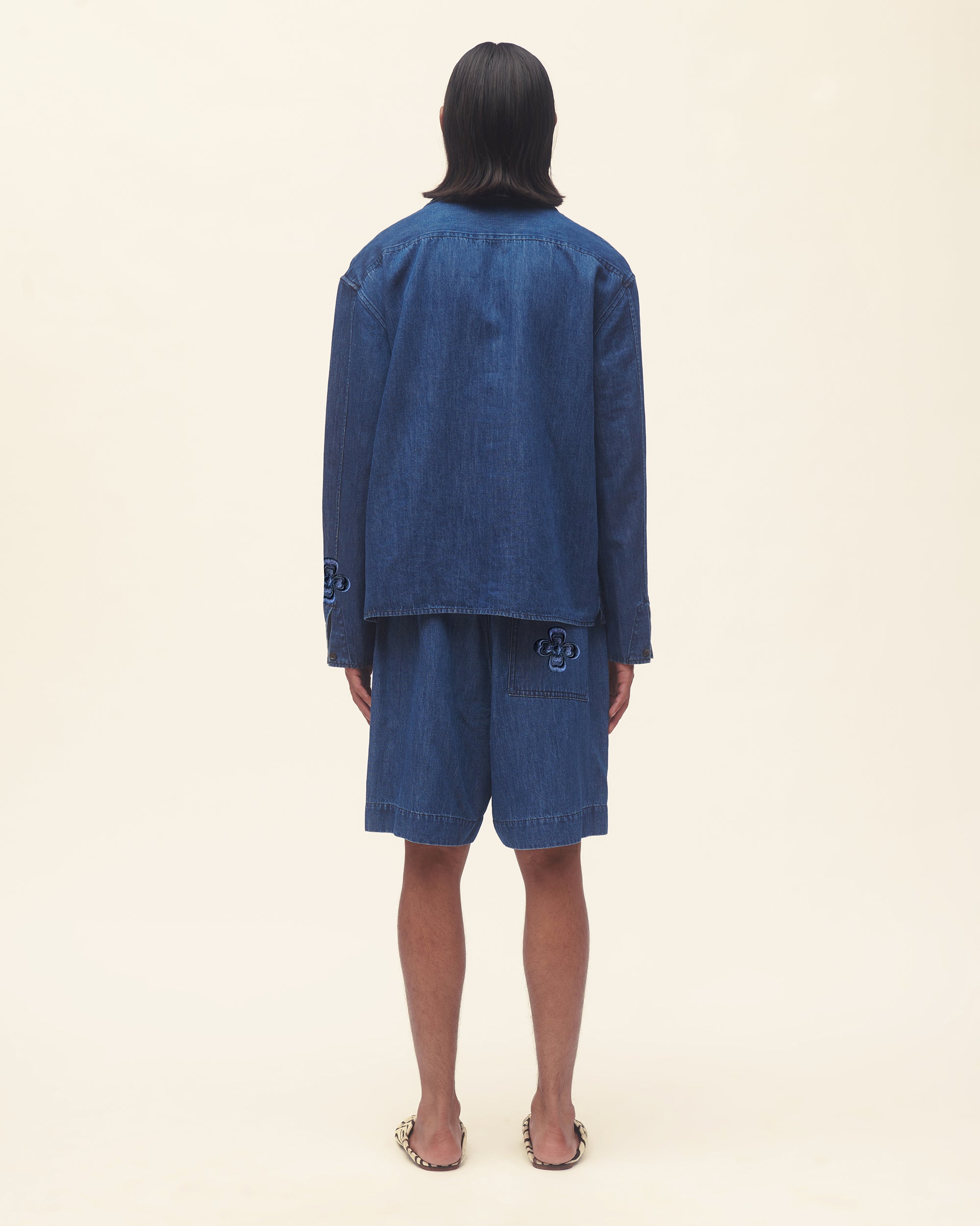 Person wearing a blue denim outfit set on a beige background