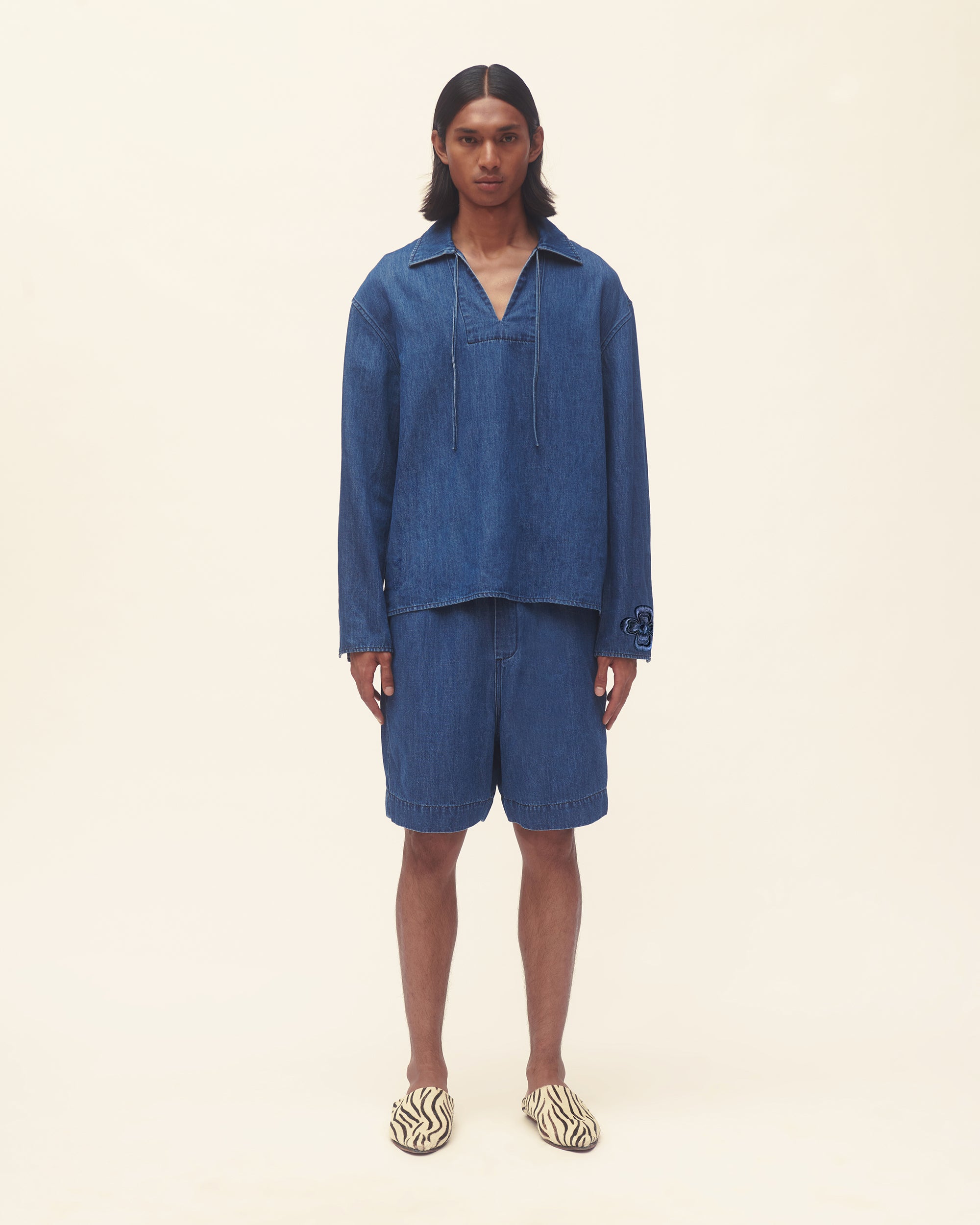 Person wearing a blue denim outfit set on a beige background