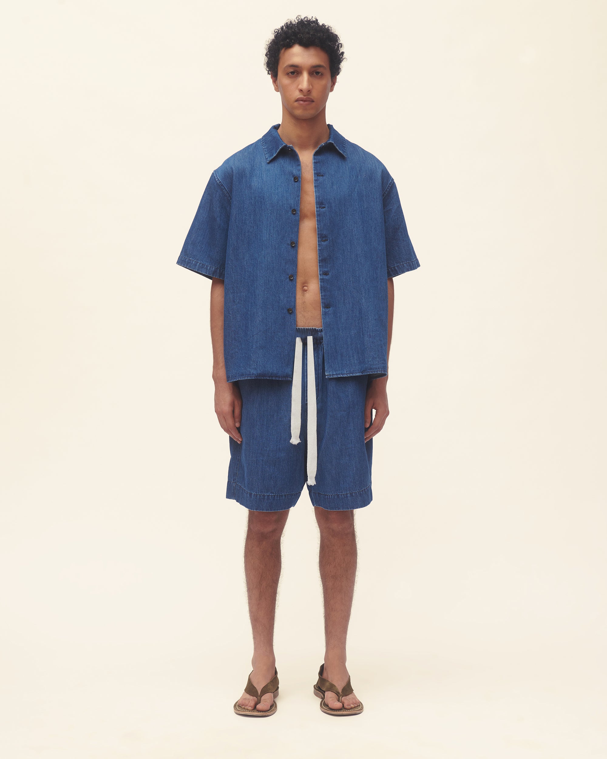Man wearing a blue denim shirt and shorts on a beige background