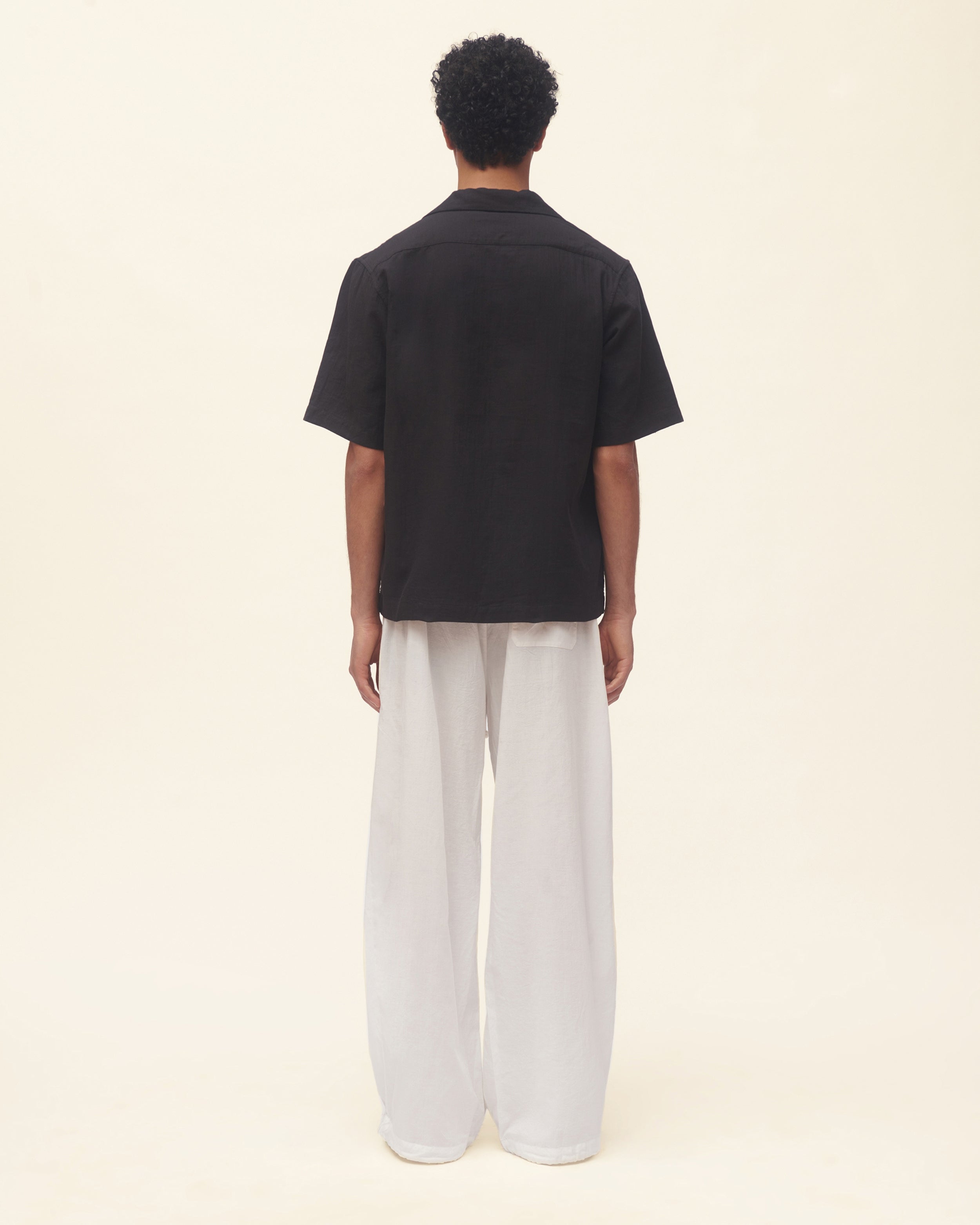 Person wearing a black shirt and white pants on a beige background