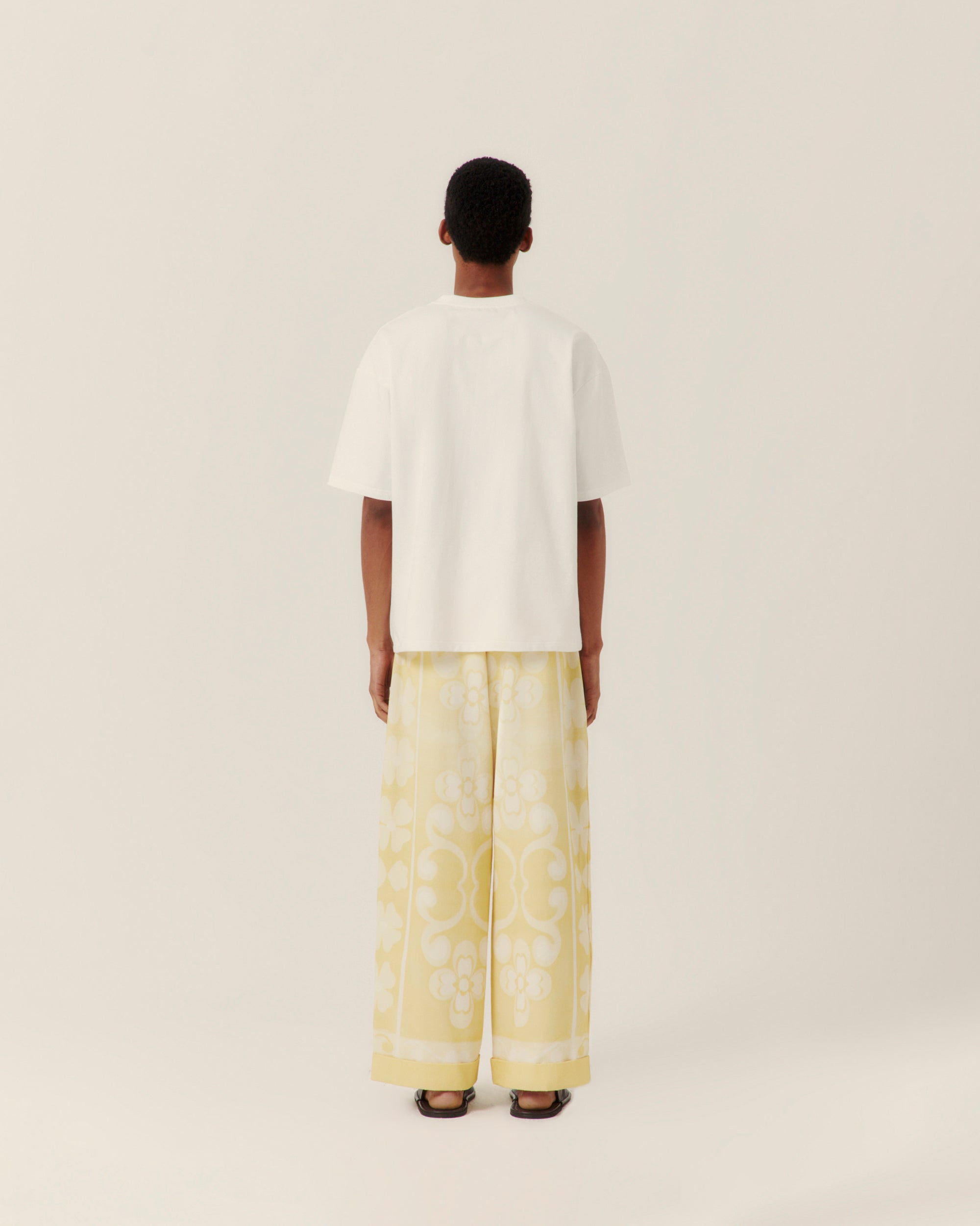 Person wearing white tee with embroidered detail against beige wall