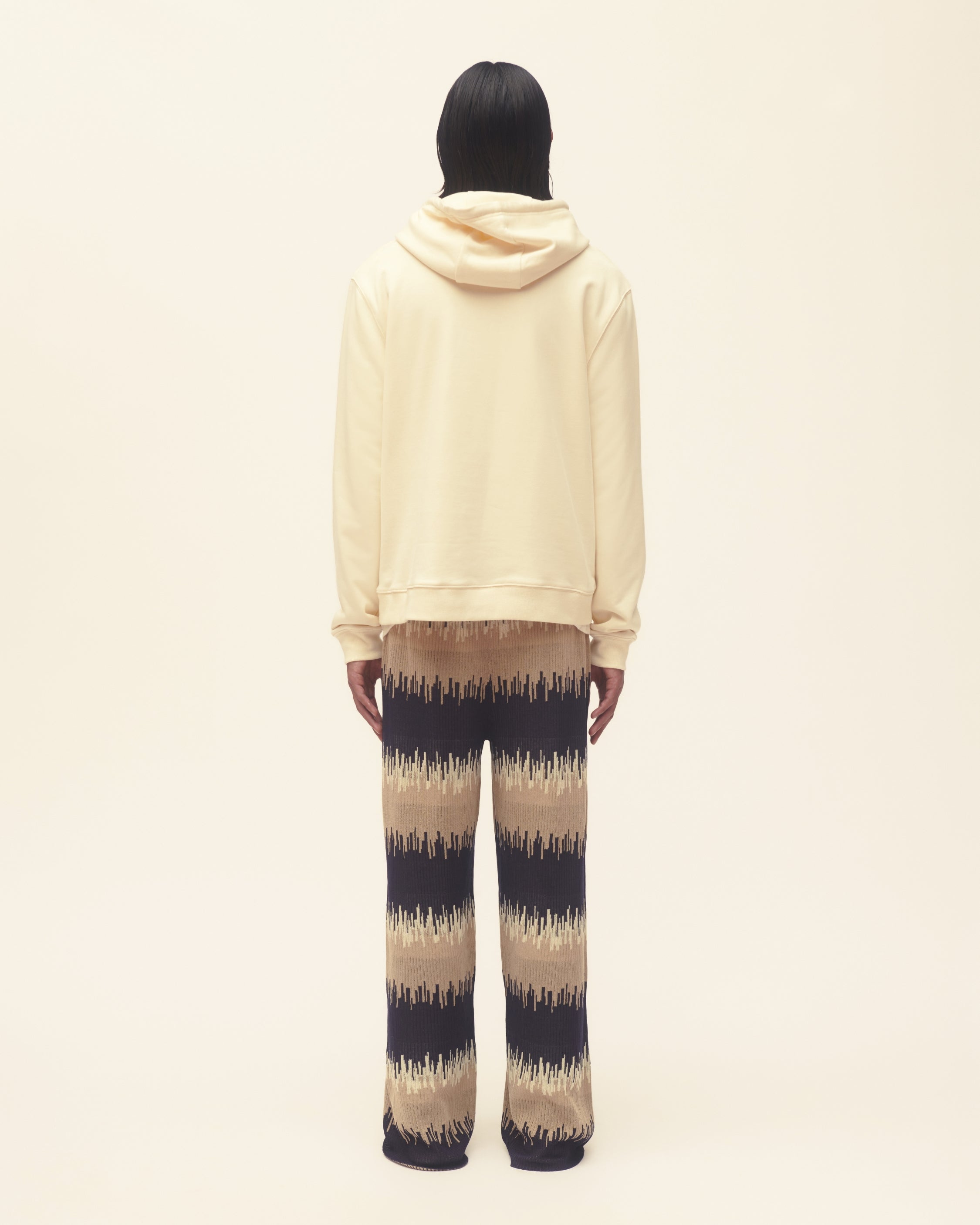 Person wearing a beige hoodie and wavy print pants on a plain background