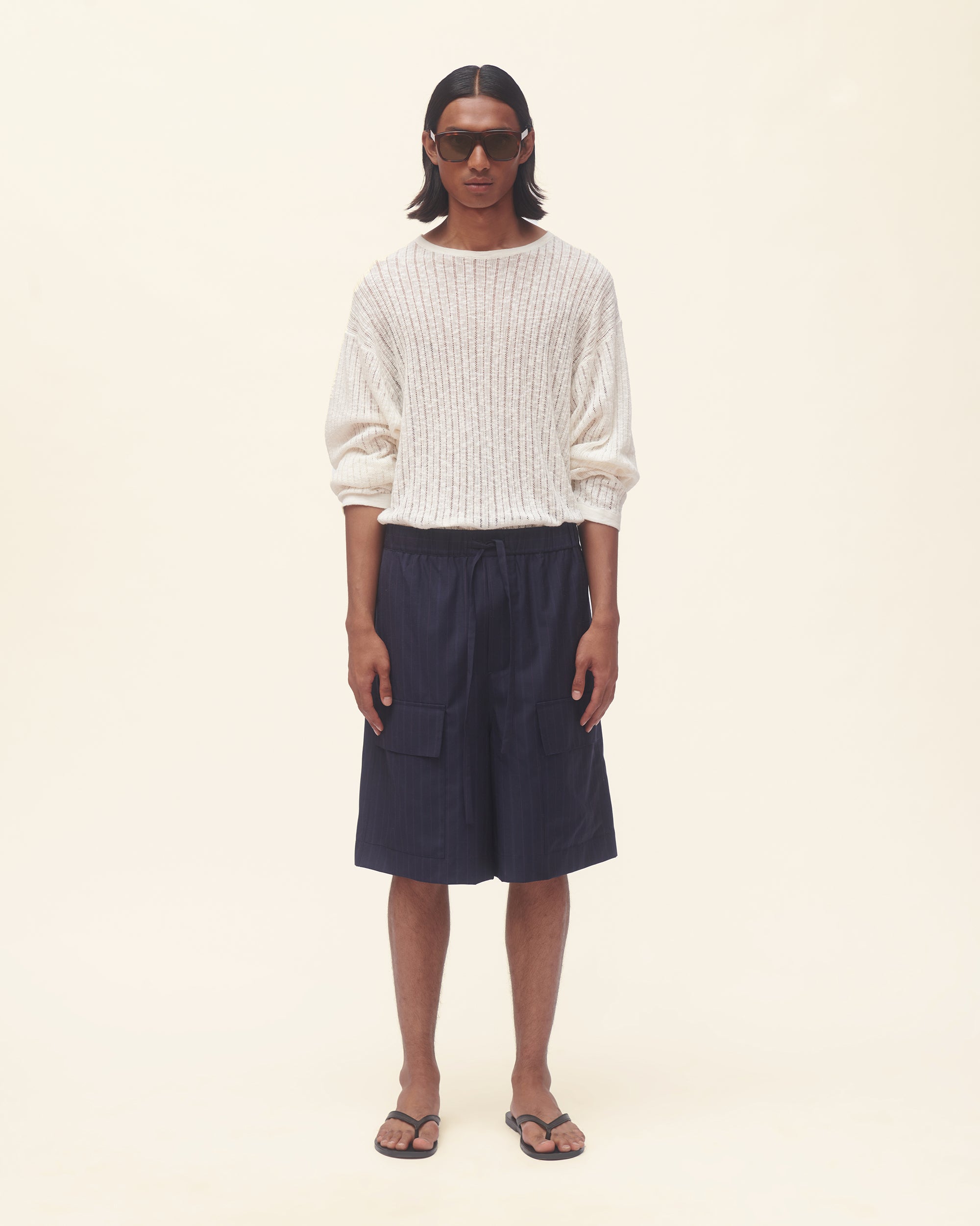 Person wearing a white sweater and navy shorts on a beige background