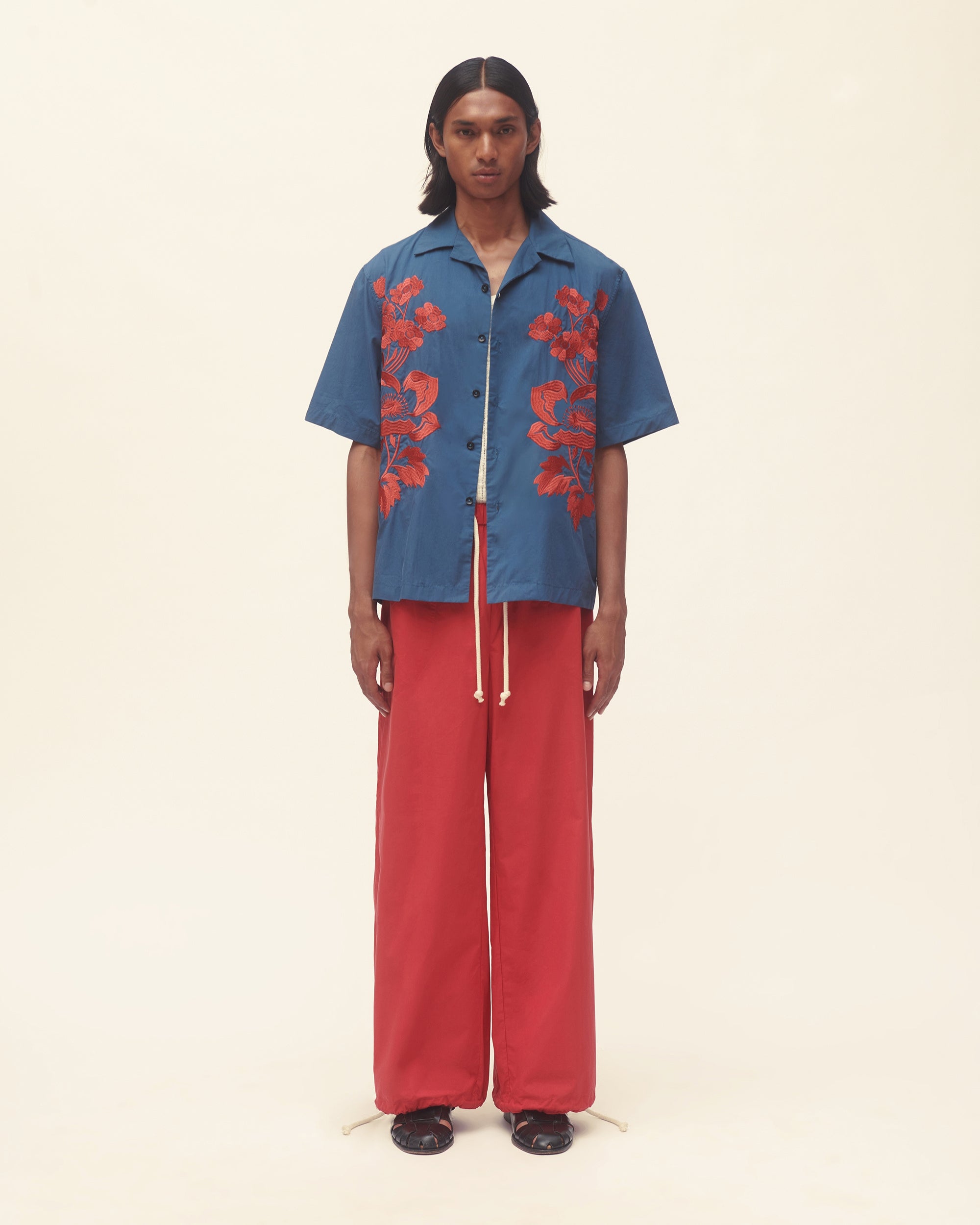 Person wearing a blue shirt with red floral patterns and red pants on a beige background