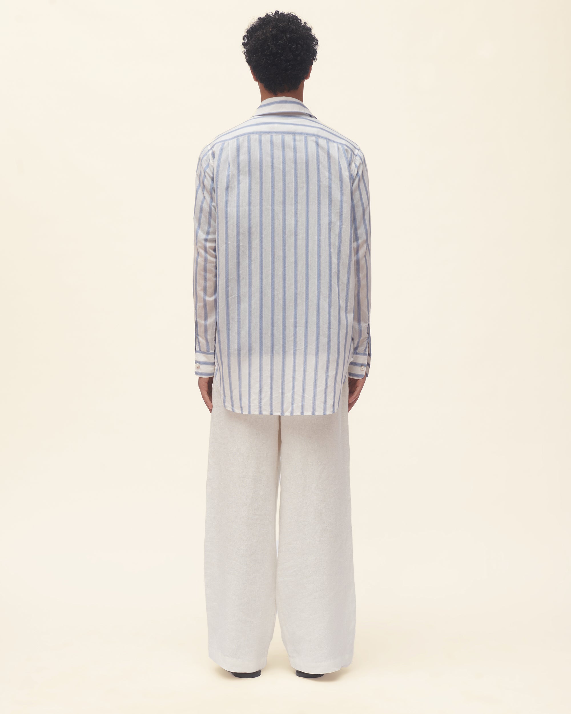 Person wearing a striped shirt and white pants on a beige background